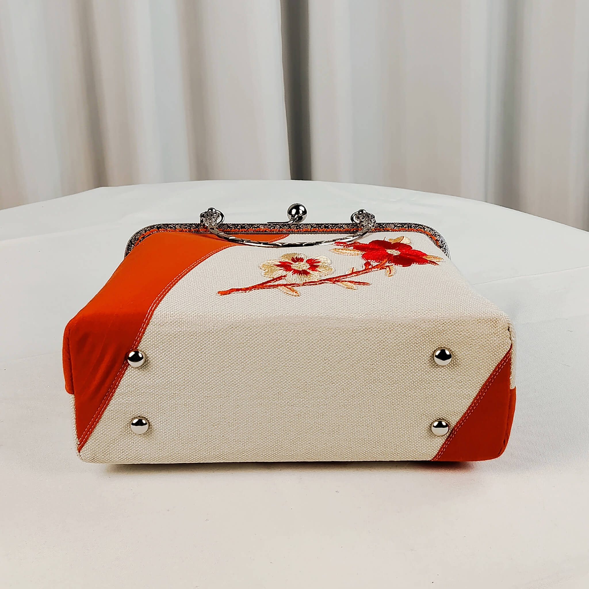Bottom view of Acever A001 clutch bag showing four protective silver metal feet studs on ivory and orange polyester base