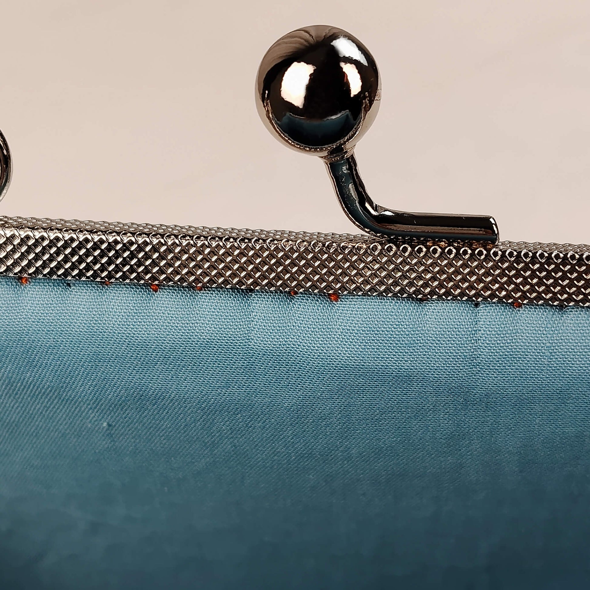 Close-up detail of Acever A001 clutch bag showing ornate engraved silver kiss-lock frame with twin ball clasp and teal polyester fabric texture