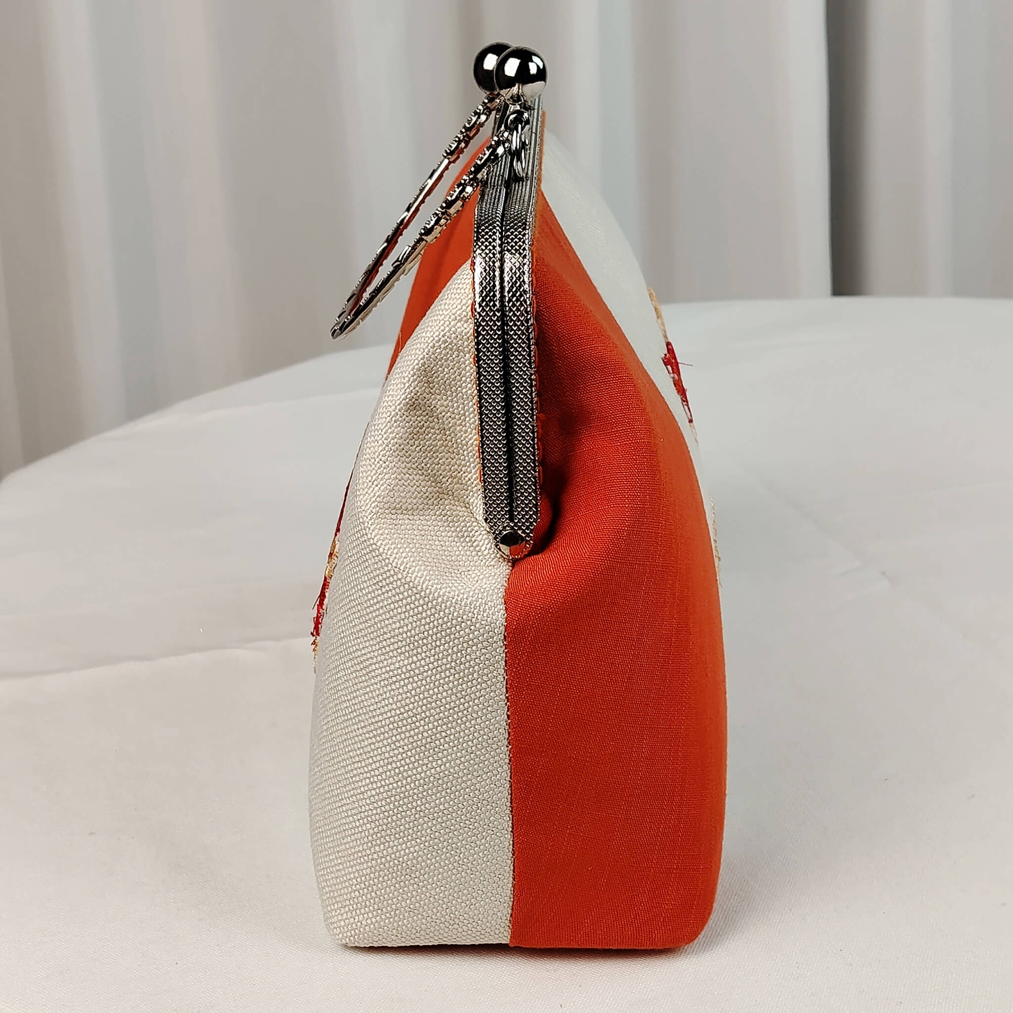 Left side view of Acever A001 clutch bag showing orange polyester panel and silver ornate kiss-lock frame edge