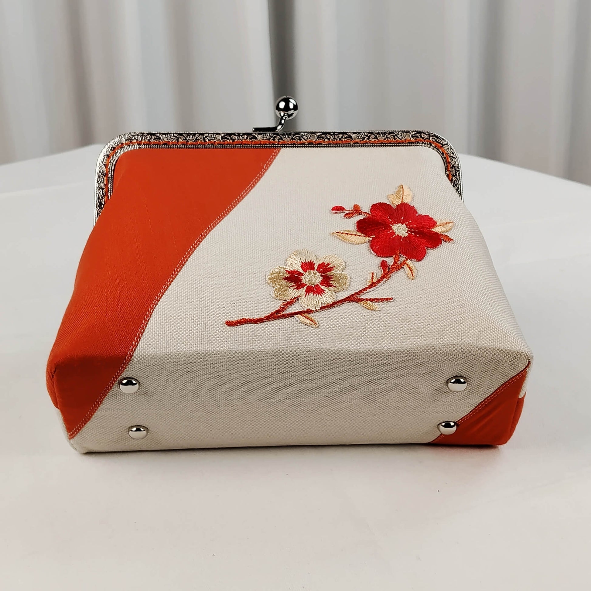 Acever A001 plum blossom clutch bag lifestyle shot on white table with autumn maple leaves and orange chrysanthemums showing full bag with silver chain handle