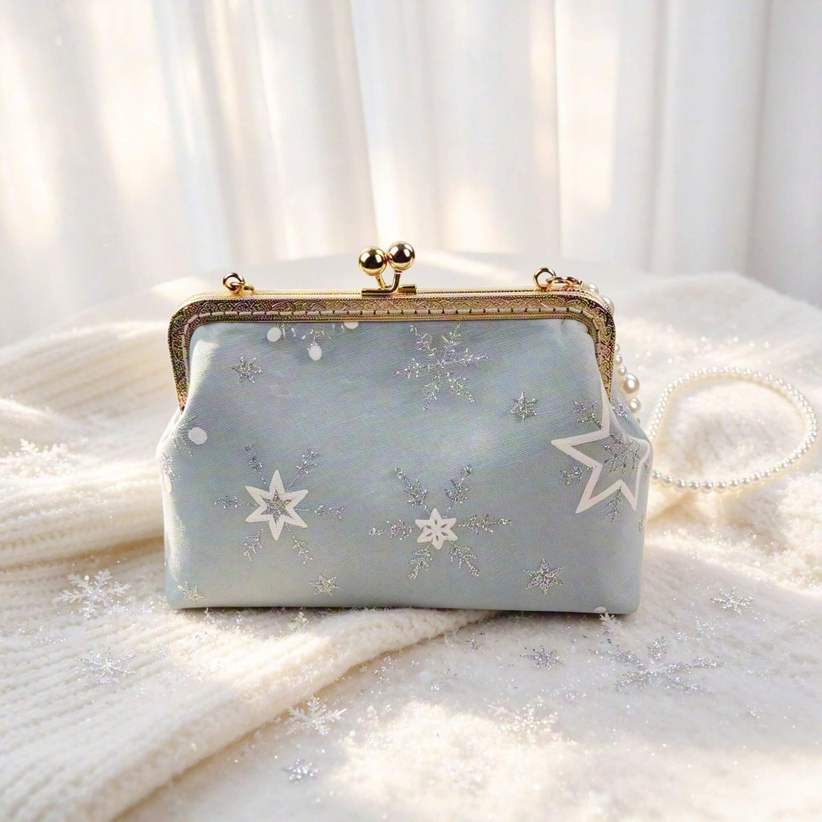 Acever A002 snowflake clutch bag lifestyle shot on white knit fabric with scattered snowflake decorations showing full bag with pearl bead strap and gold kiss-lock frame