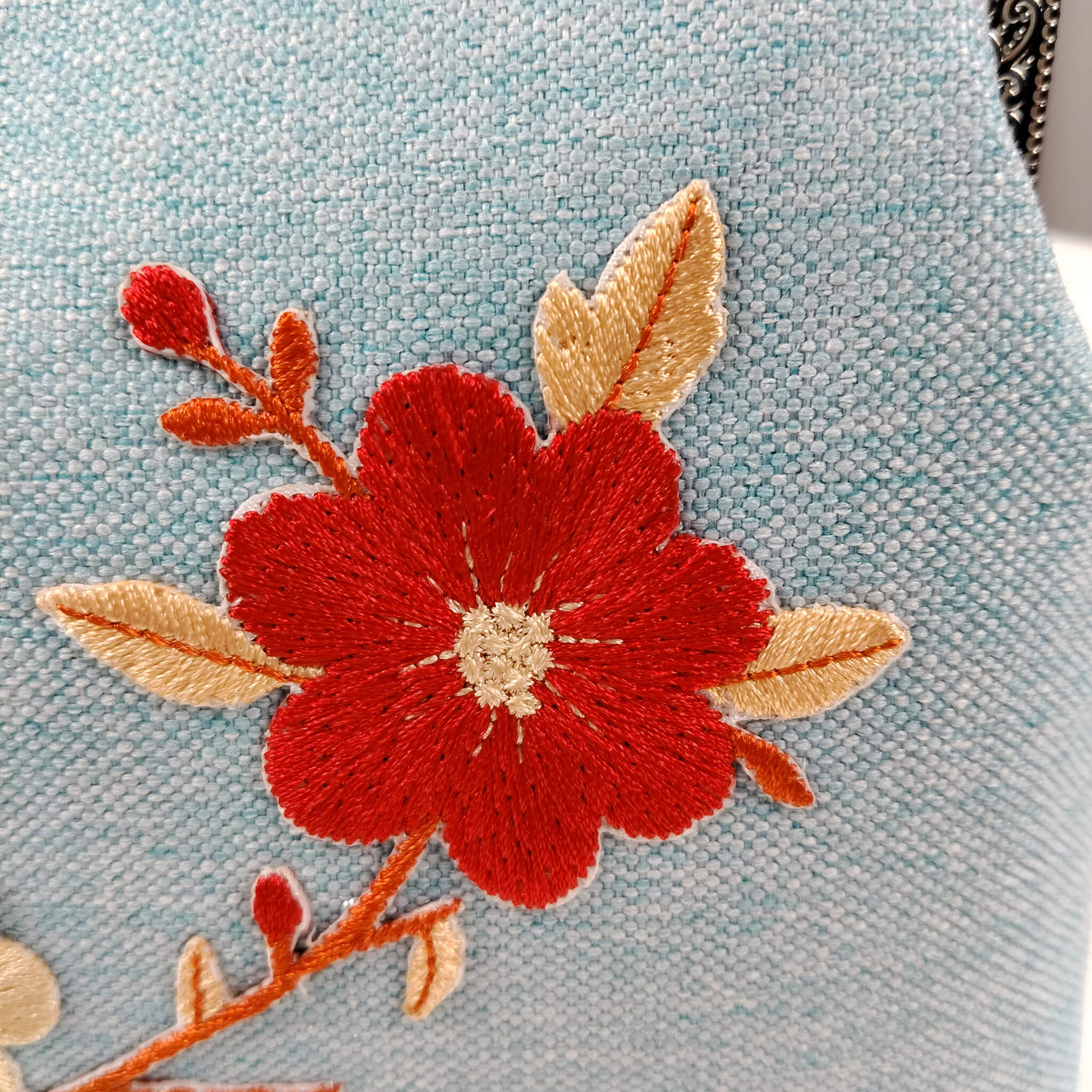 Close-up detail of Acever A003 clutch bag showing red and cream cherry blossom embroidery with gold leaves on powder blue linen-texture polyester fabric