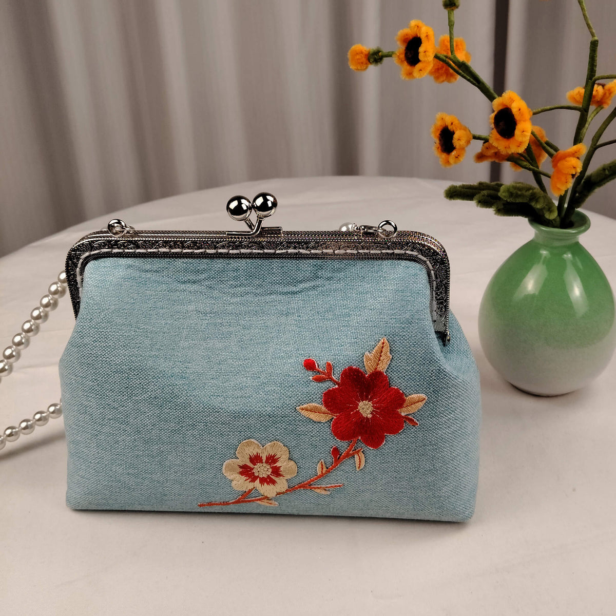 Acever A003 cherry blossom clutch bag lifestyle shot showing side angle with silver zipper detail pearl bead crossbody strap and red floral embroidery on powder blue polyester body