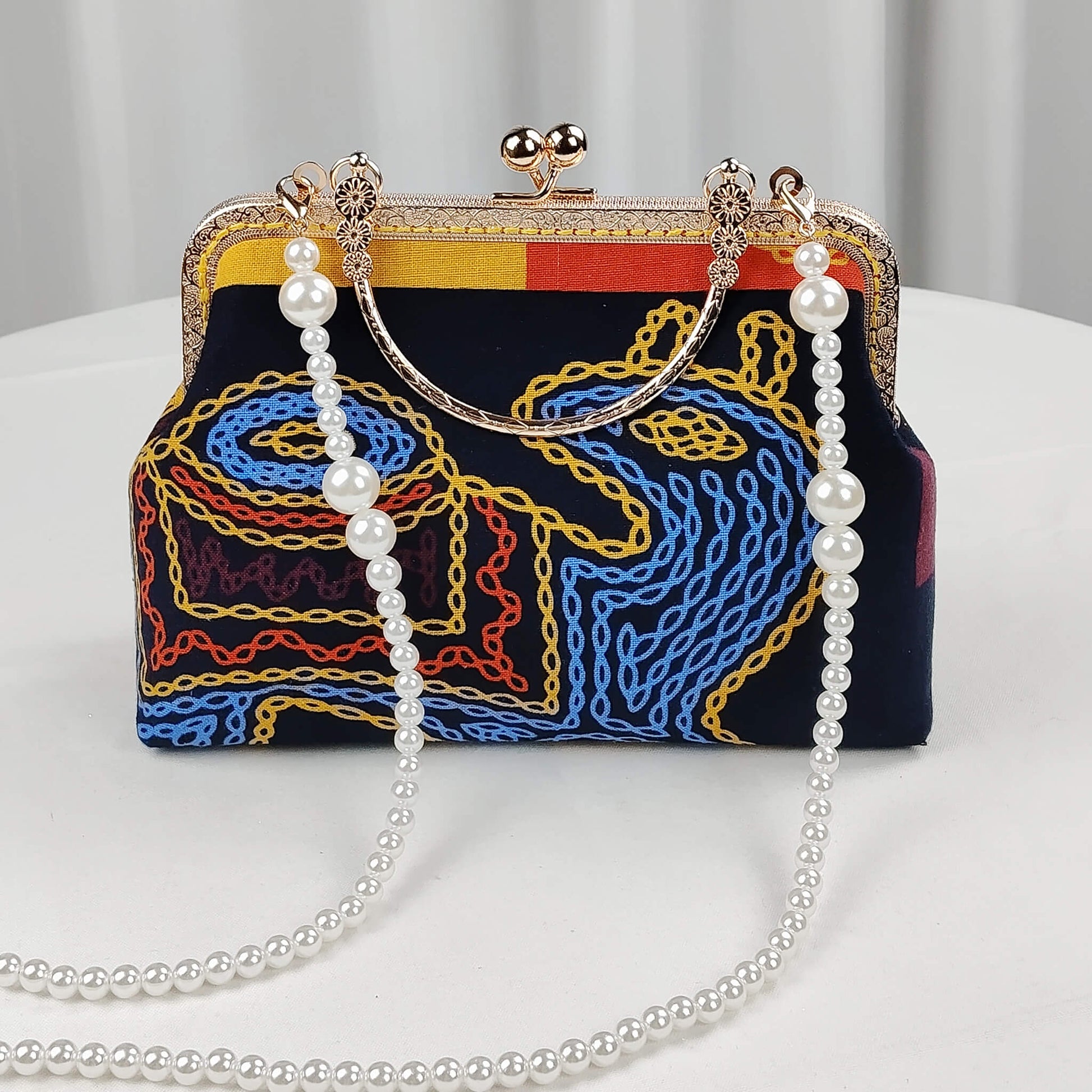 Acever A004 abstract chain clutch bag lifestyle shot on white marble surface with pearl bead crossbody strap laid out showing full front view with gold kiss-lock frame and chain-link embroidery