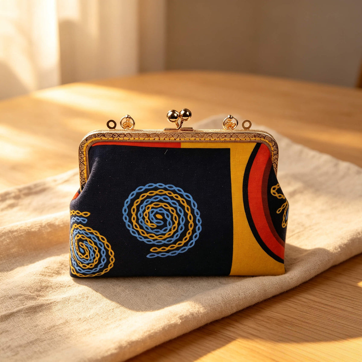 Acever A004 abstract chain clutch bag lifestyle shot on wooden table in warm sunlight showing navy body with swirling chain-link embroidery and gold kiss-lock frame without strap