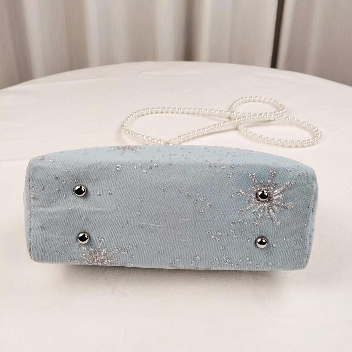 Bottom view of Acever B001 snowflake embroidered clutch bag showing ice blue polyester base with sheer tulle overlay and scattered silver snowflake and star dot accents