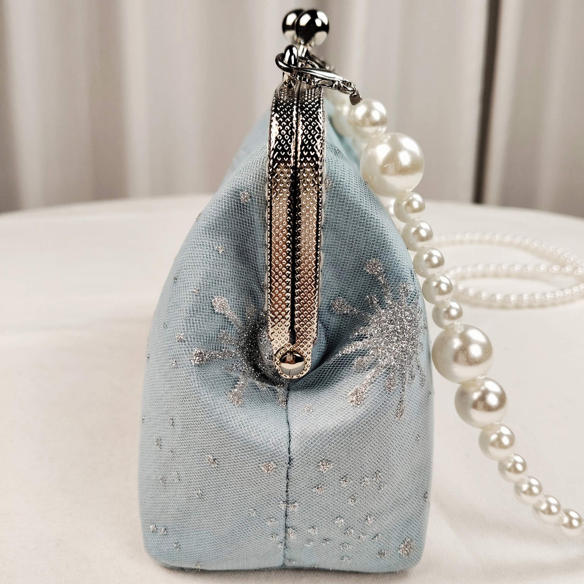 Side view of Acever B001 snowflake embroidered clutch bag showing ice blue polyester gusset with sheer tulle overlay silver snowflake accents and silver textured zipper side detail with large pearl bead strap