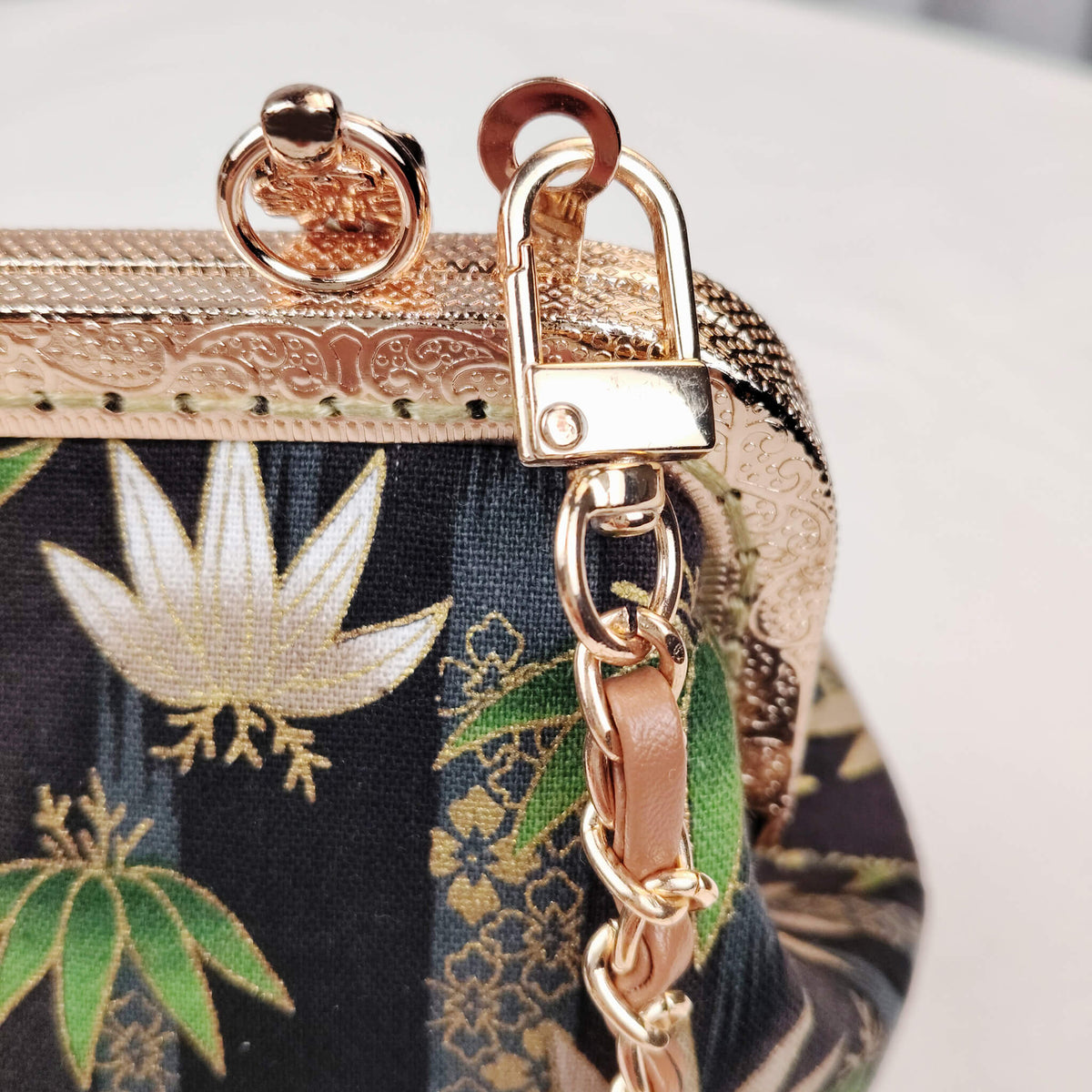 Close-up detail of Acever B002 bag showing white and gold lotus flower with green palm leaves and golden foliage on midnight navy jacquard fabric with metallic gold thread highlights
