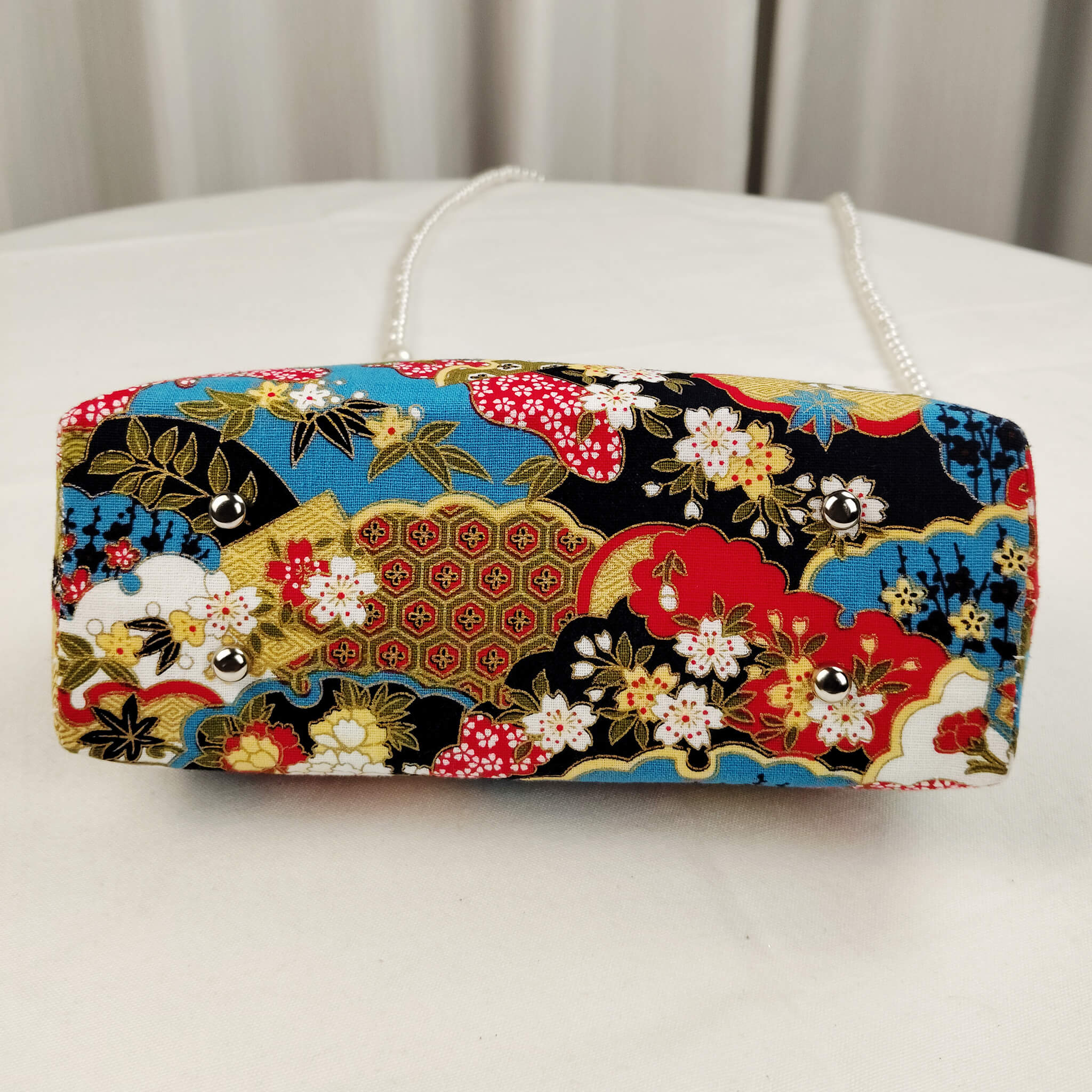 Bottom view of Acever B003 Japanese Nishiki brocade top handle bag showing black base with all-over teal blue golden yellow red cherry blossom and cloud brocade print