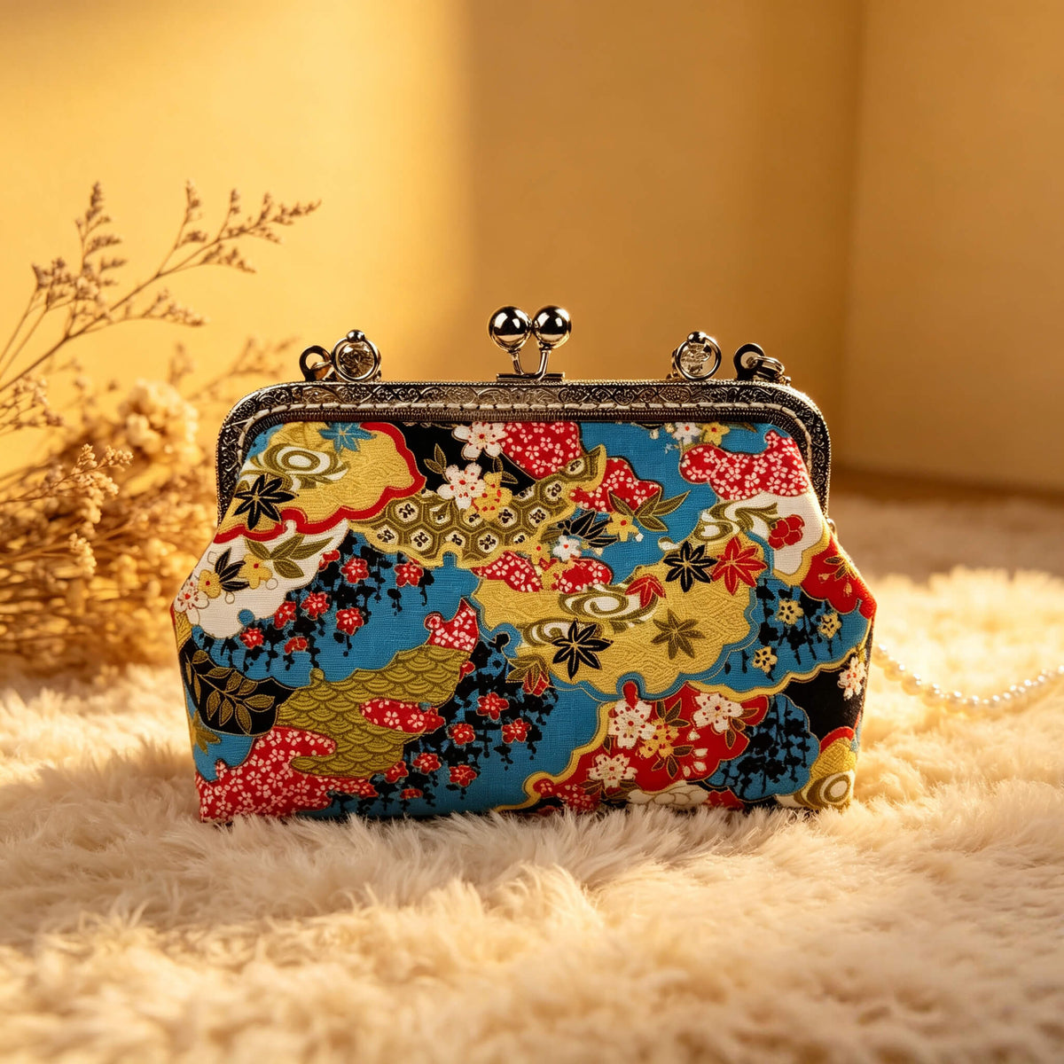 Acever B003 Japanese Nishiki brocade top handle bag lifestyle shot on white fluffy rug beside dried golden grass in warm amber light showing full front view with antique silver kiss-lock frame and pearl bead strap