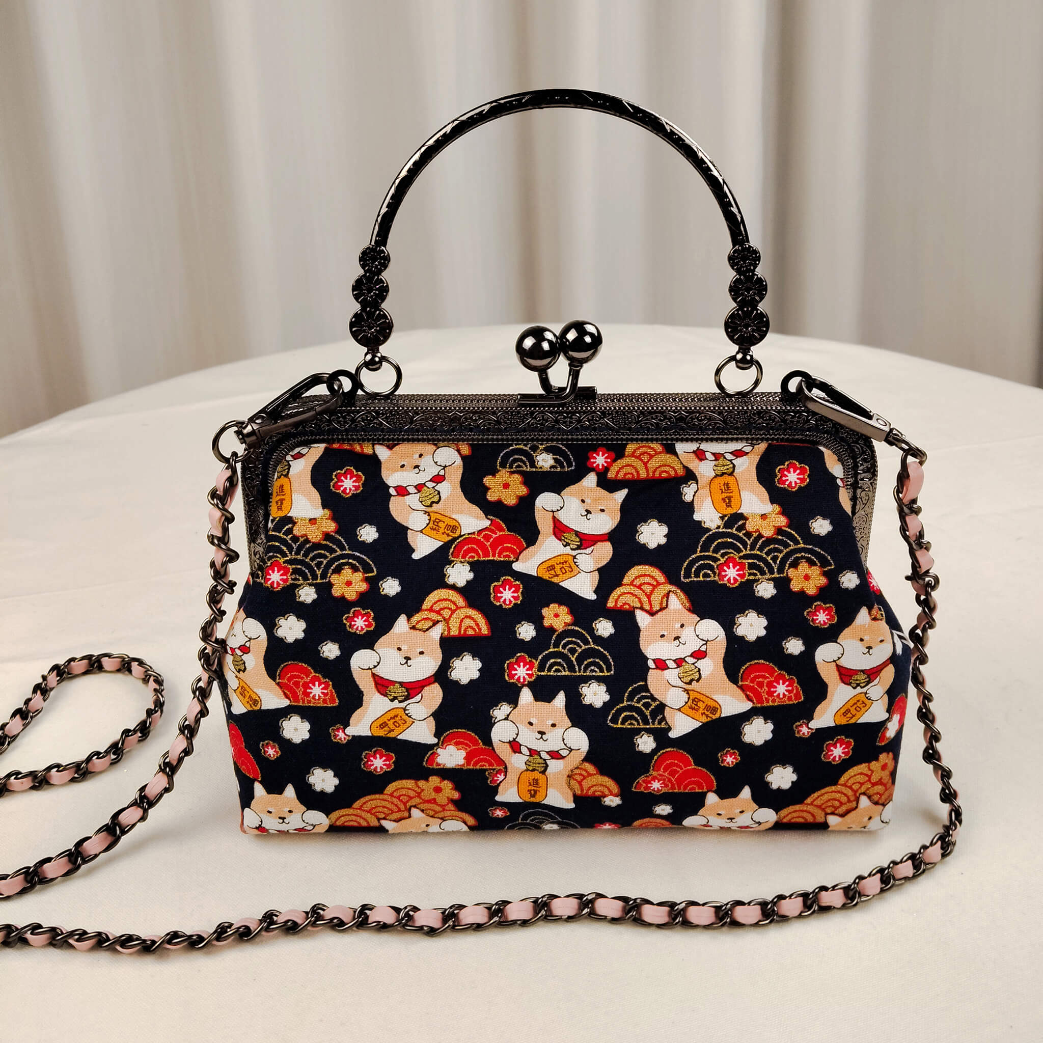 Acever B005 Lucky Shiba Inu top handle bag lifestyle shot on white surface against grey curtain backdrop showing front view with gunmetal ornate filigree kiss-lock frame decorative top handle and blush pink woven chain strap