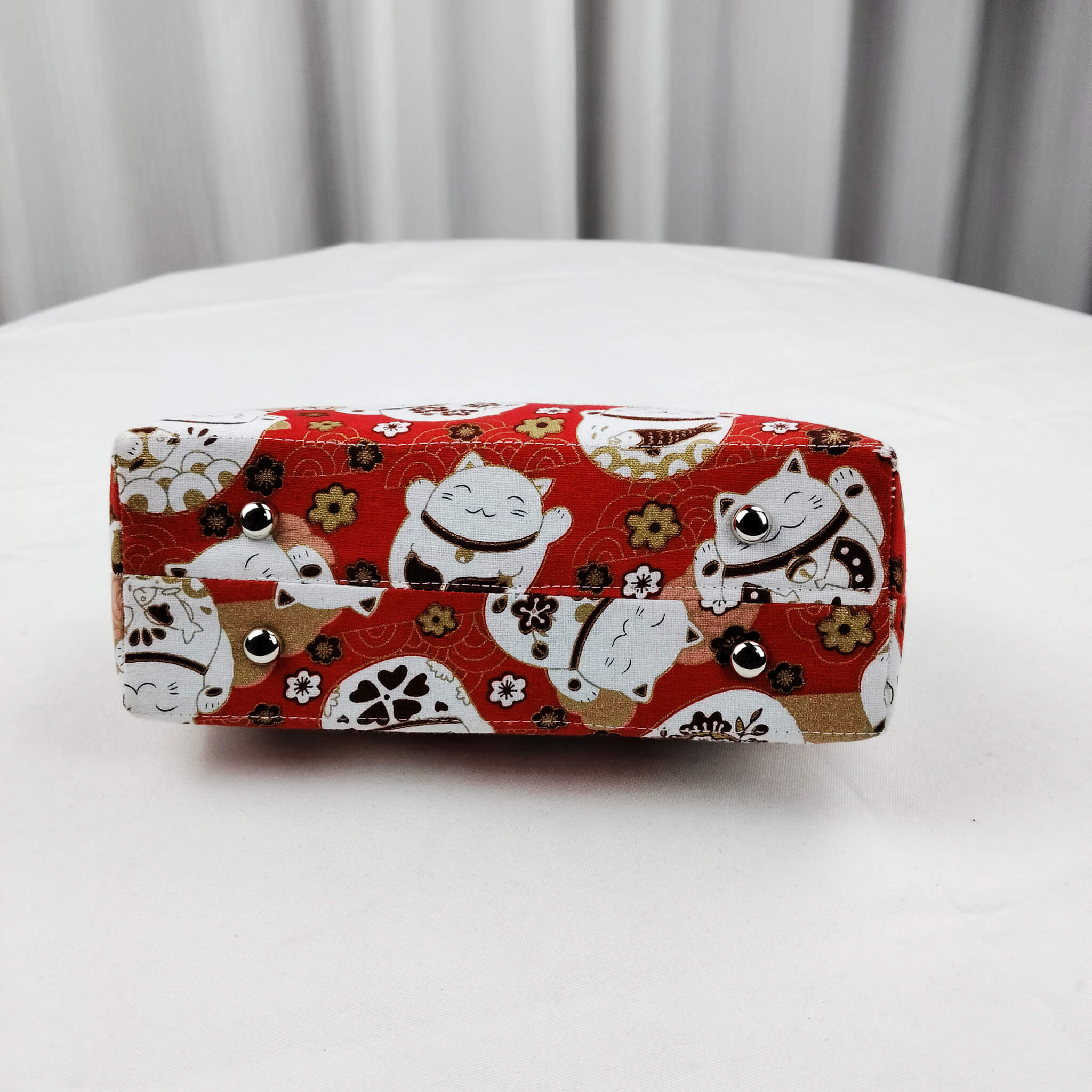 Bottom view of Acever B006 Lucky Cat Maneki-Neko top handle bag showing vivid red polyester base with all-over white lucky cats plum blossoms and seigaiha wave print with golden metallic thread highlights