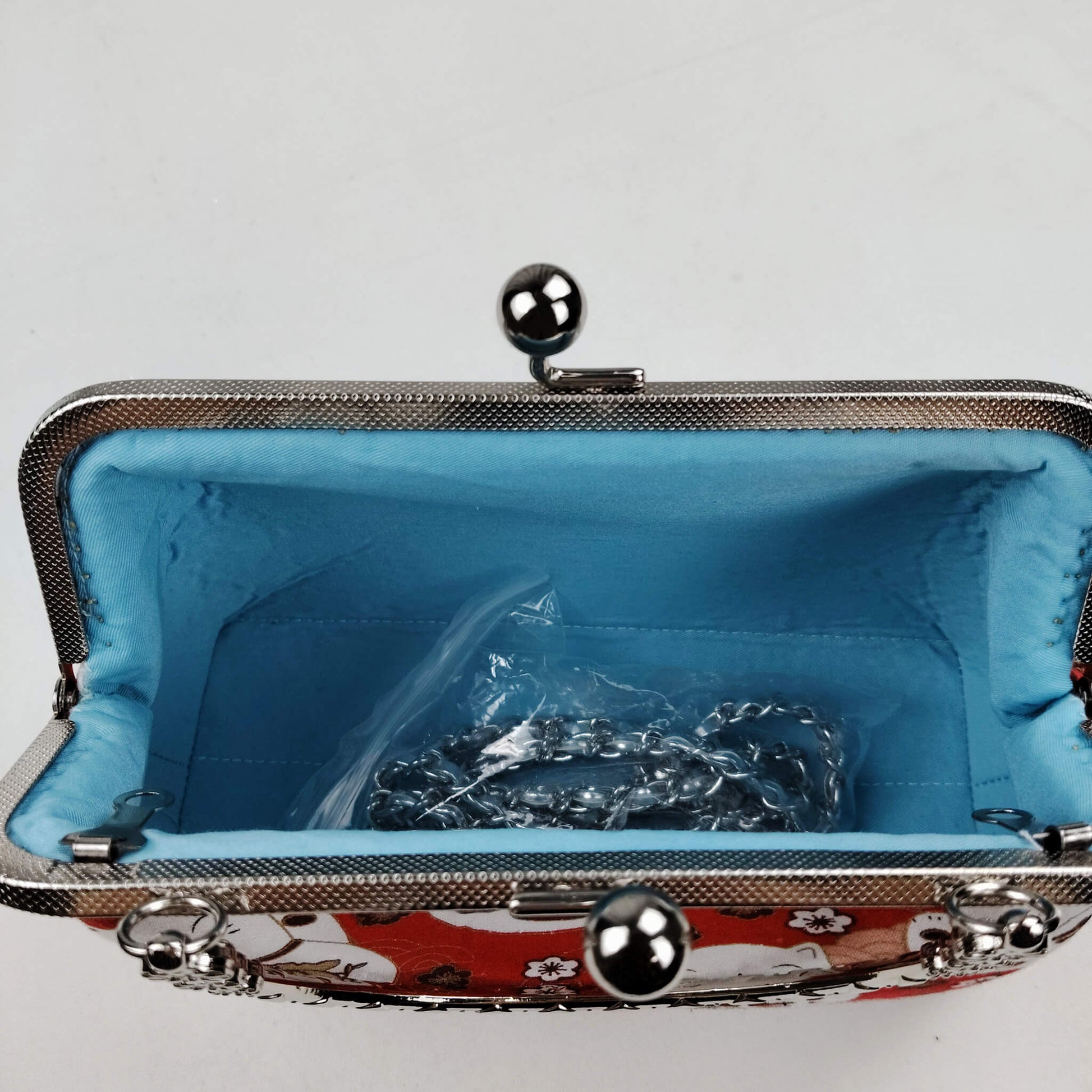Interior view of Acever B006 Lucky Cat Maneki-Neko bag open showing sky blue smooth satin lining with single open compartment and gunmetal double twin ball clasp frame edge with flat-link chain strap stored inside