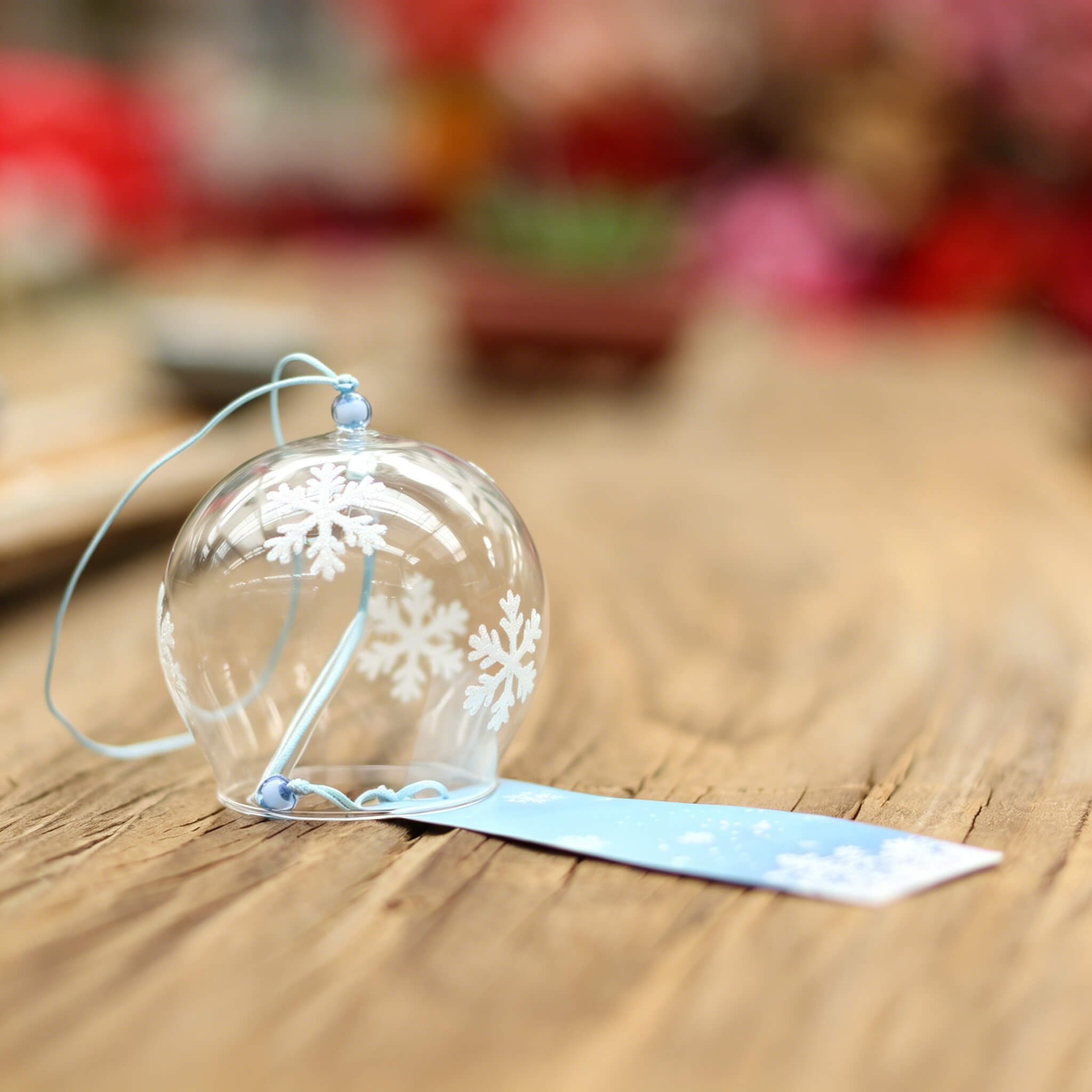 Acever white snowflake glass wind chime X07 resting on wooden surface showing flat-rim clear globe with white snowflake pattern and blue paper strip