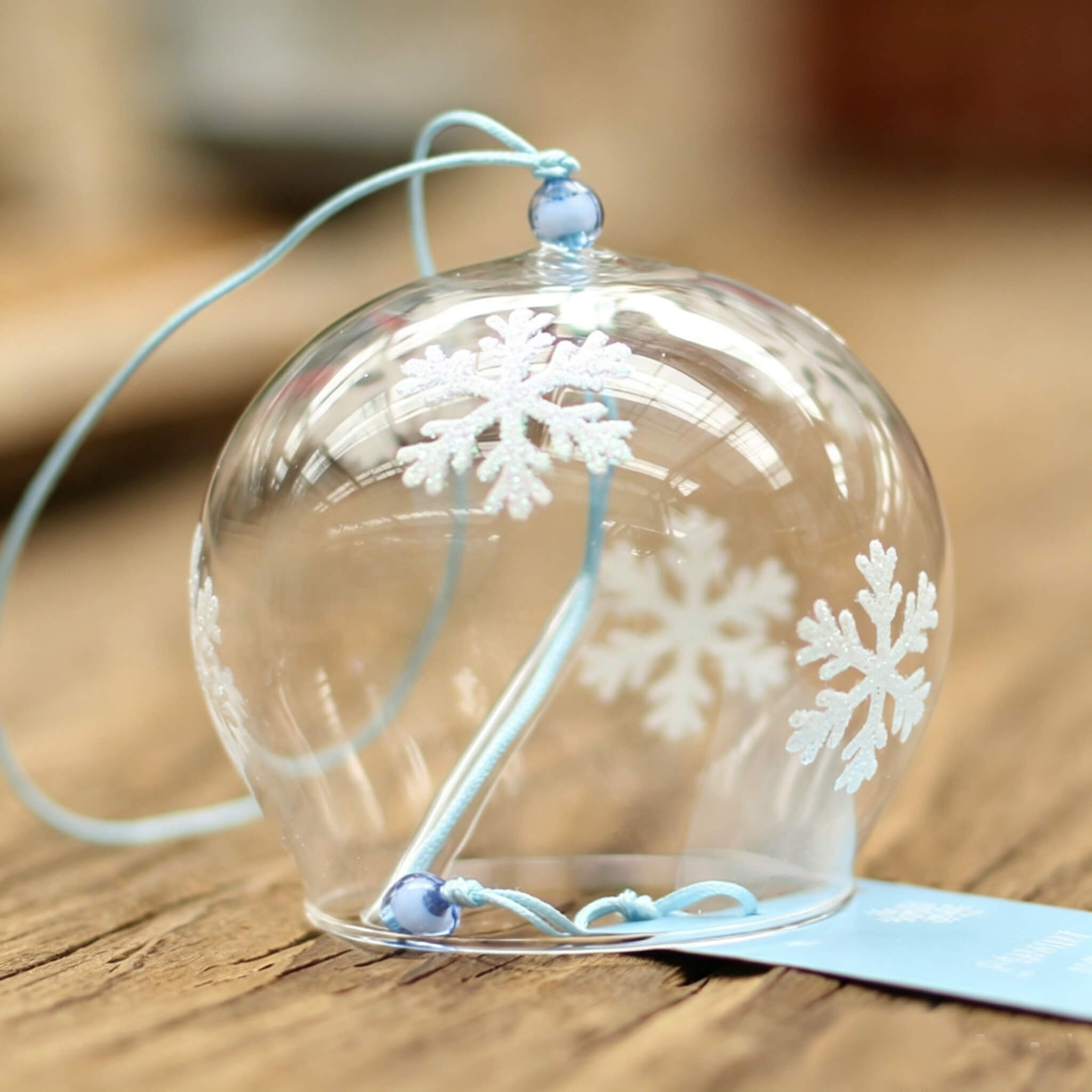 Close-up of Acever snowflake glass wind chime X07 hanging showing flat-rim clear globe with white snowflake motifs and sky-blue cord