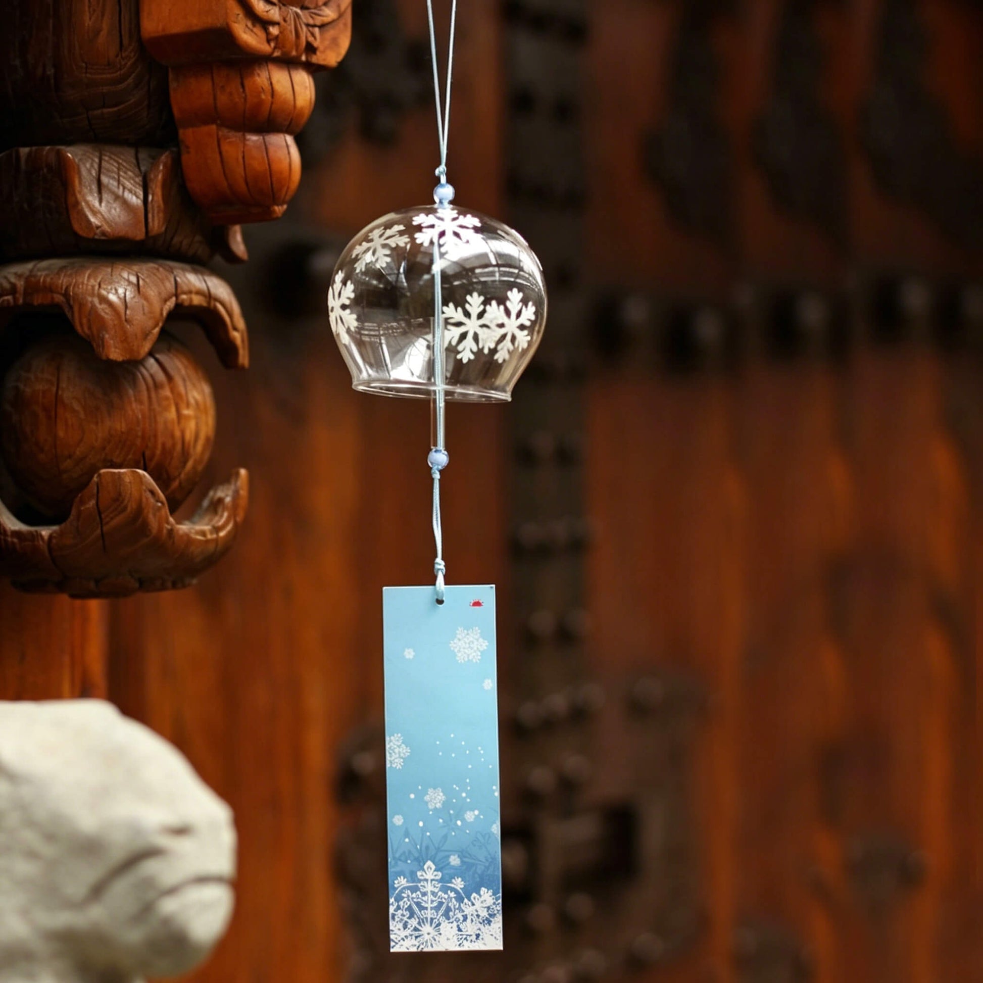 Acever white snowflake glass wind chime X07 hanging against traditional wooden architecture with blue snowflake paper strip swaying