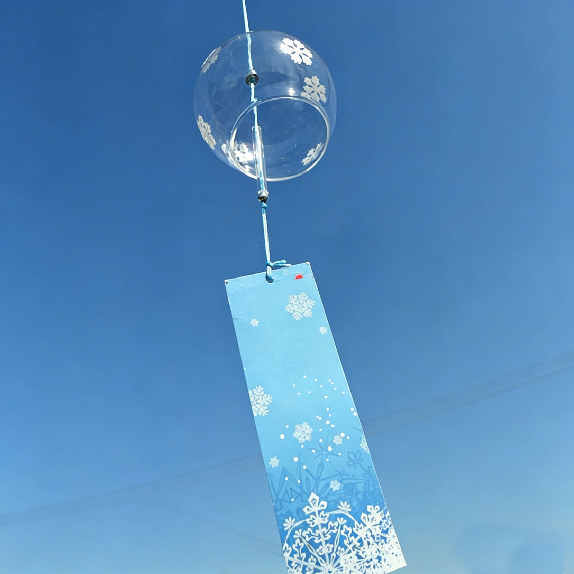 Acever white snowflake glass wind chime X07 hanging against blue sky showing clear globe with snowflake pattern and blue paper strip