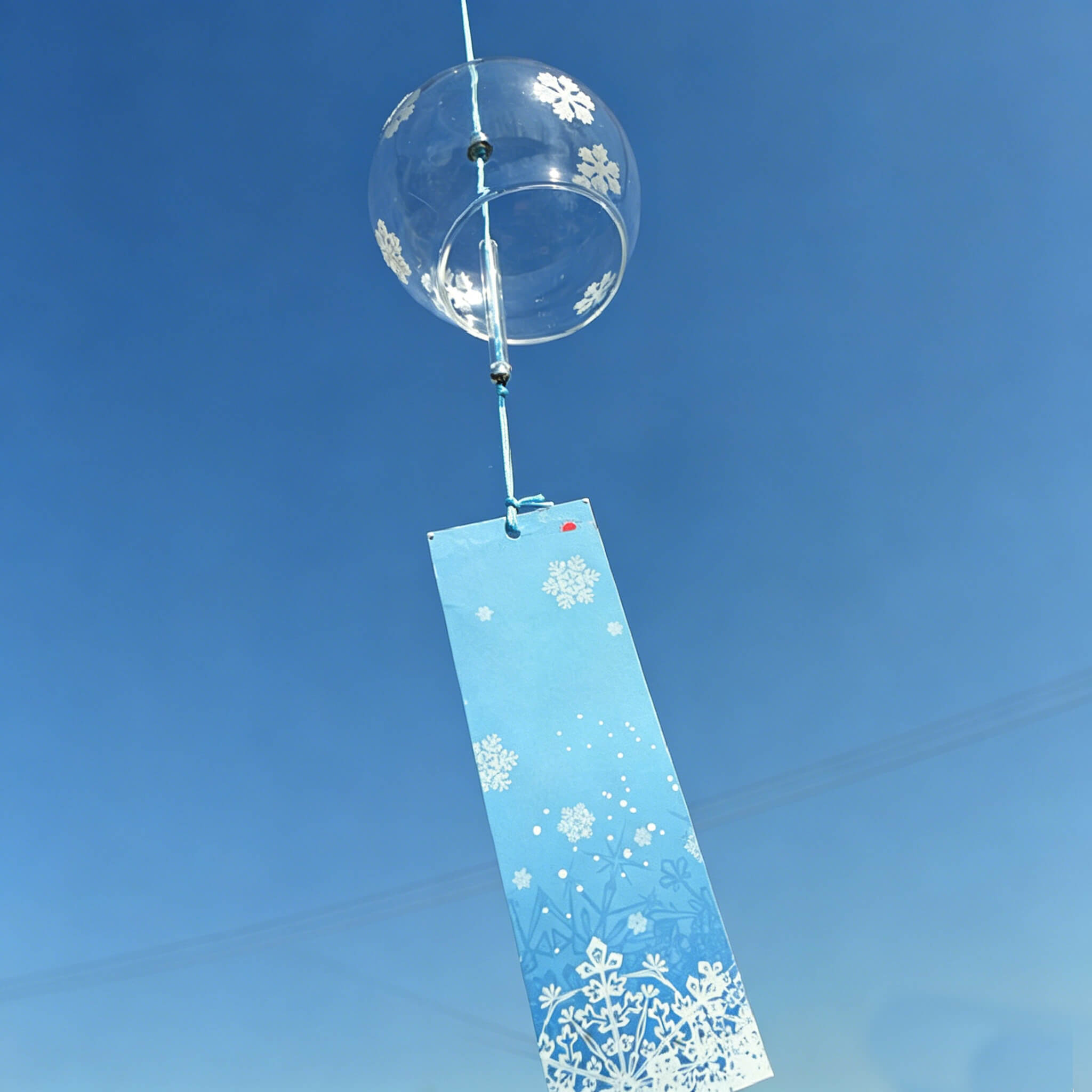 Acever white snowflake glass wind chime X07 hanging against blue sky showing clear globe with snowflake pattern and blue paper strip