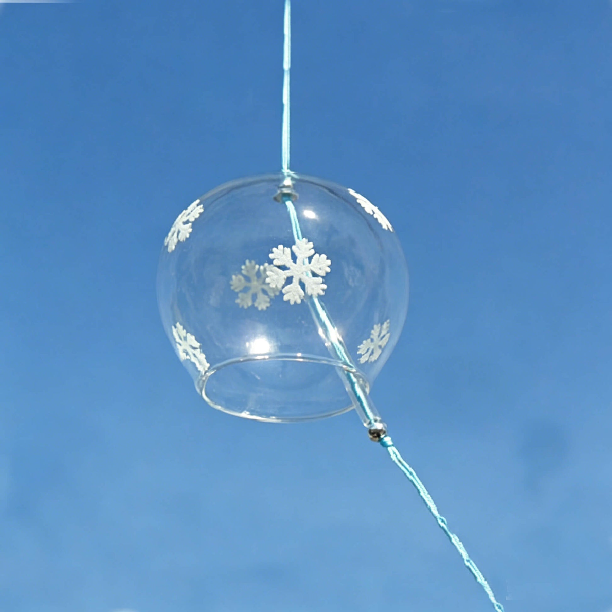 Right side view of Acever white snowflake glass wind chime X07 against blue sky showing round clear globe with snowflake motifs and blue cord