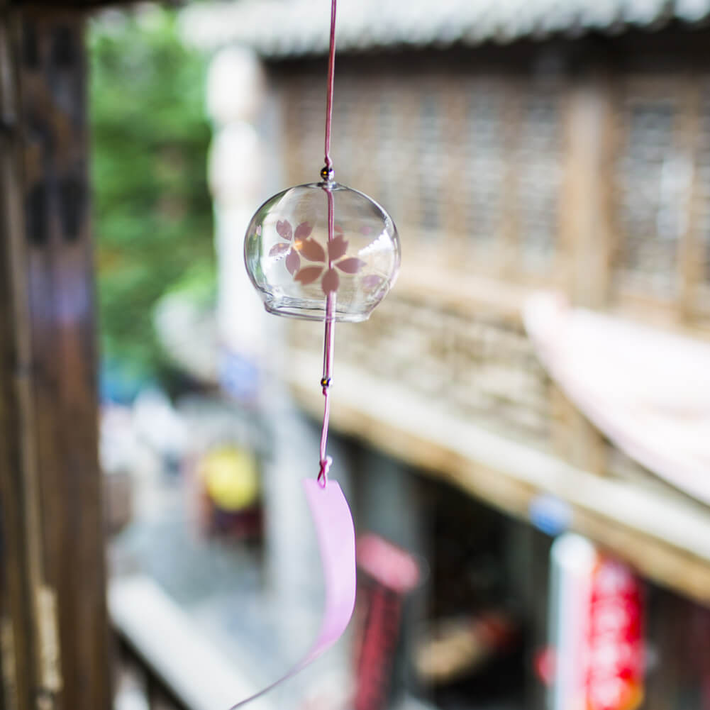 Acever pink sakura glass wind chime X09 hanging from wooden beam in traditional Japanese setting with deep rose sakura paper strip
