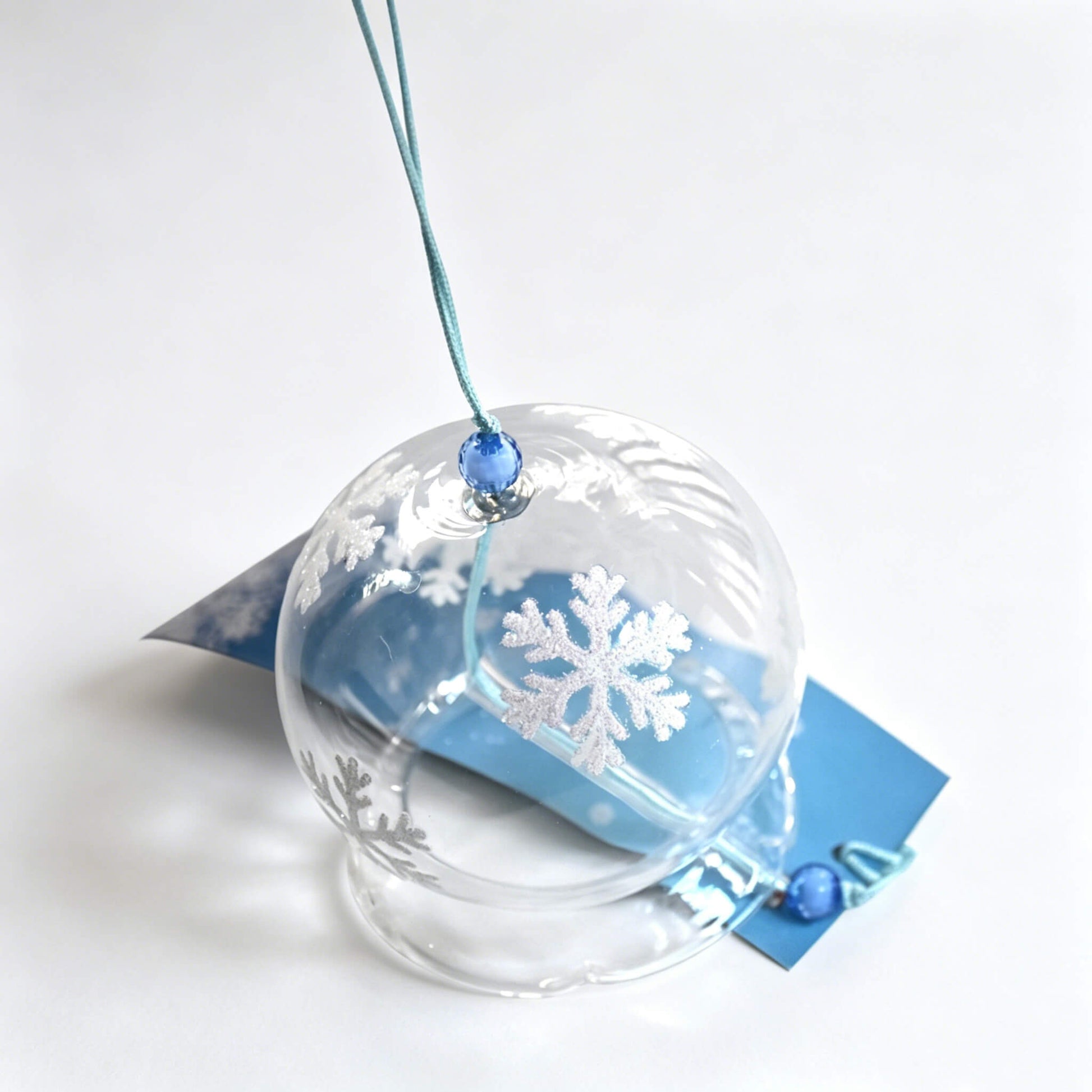 Acever white snowflake waved-rim glass wind chime X10 resting on white surface showing scalloped edge globe with blue bead and snowflake paper strip