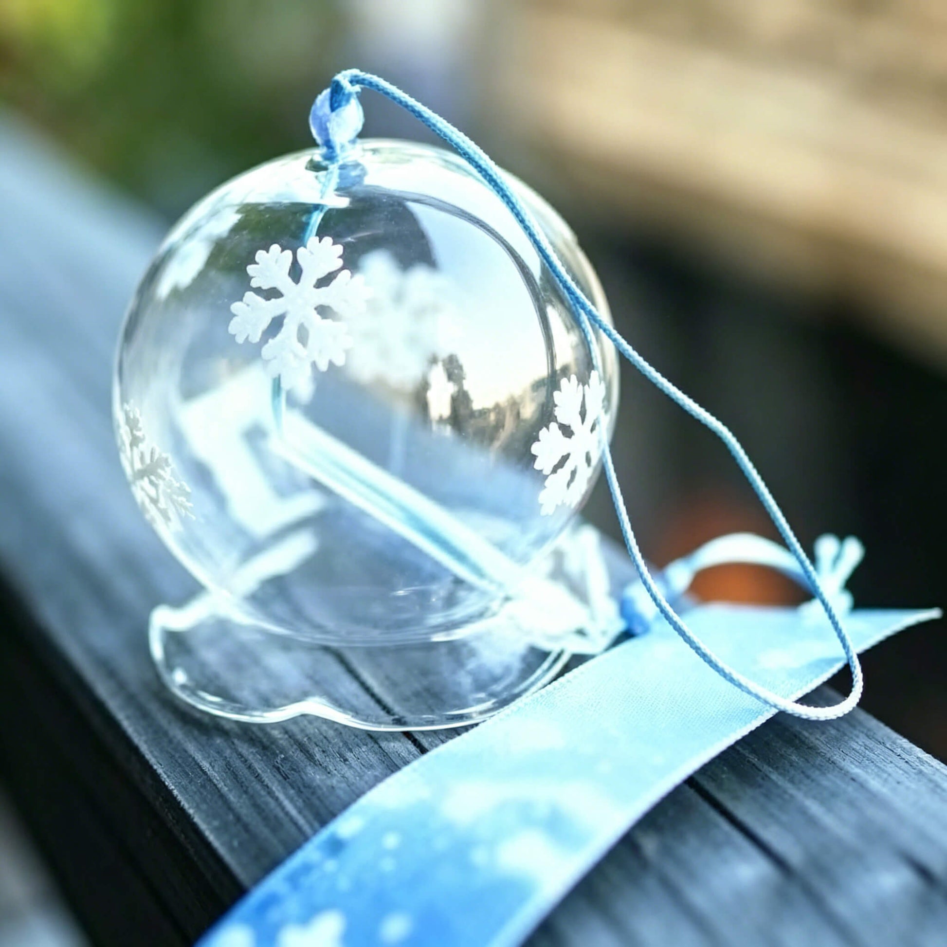 Detail shot of Acever snowflake waved-rim glass wind chime X10 resting on wooden rail with blue snowflake paper strip and sky-blue cord