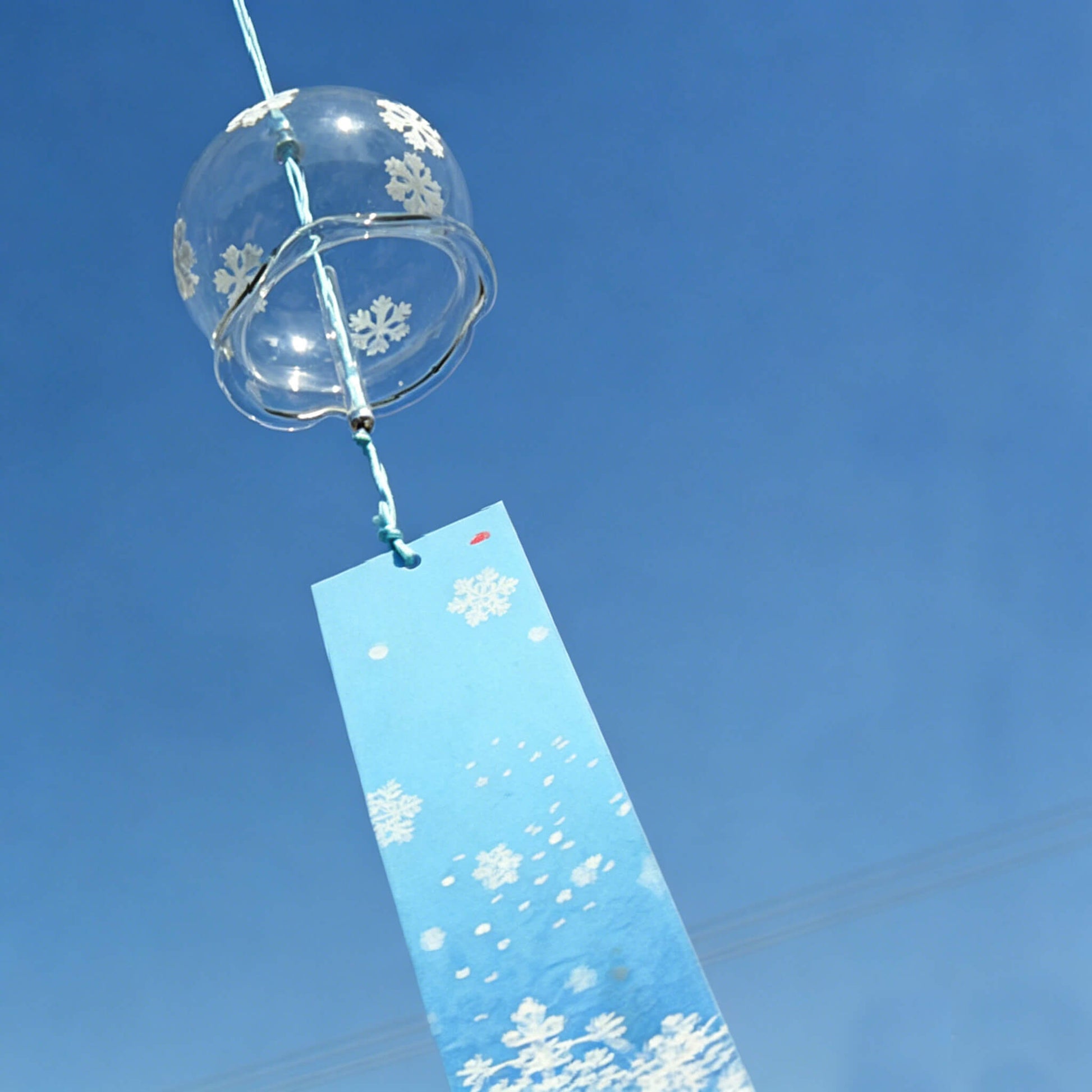 Acever white snowflake waved-rim glass wind chime X10 hanging against blue sky showing full length with blue snowflake paper strip