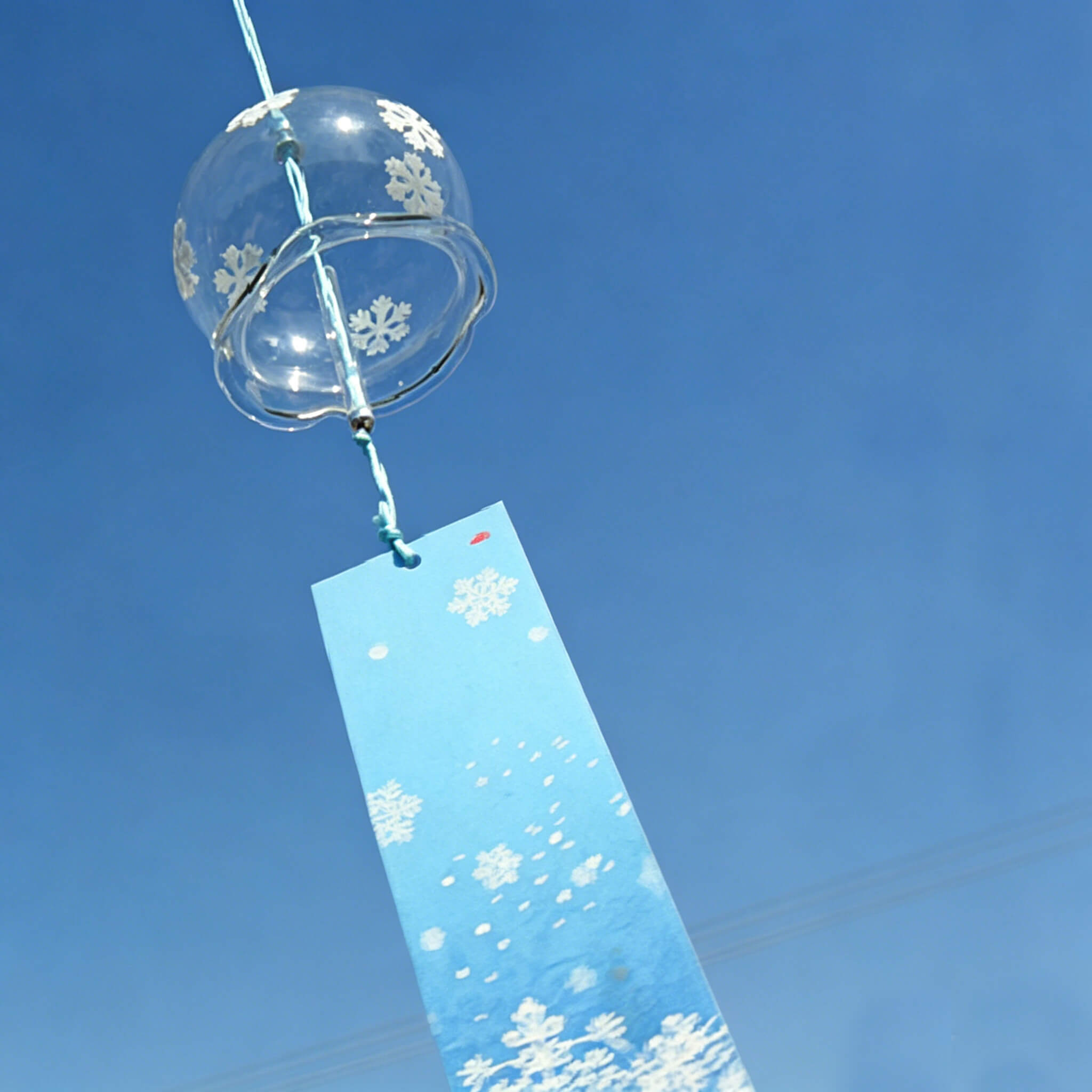 Acever white snowflake waved-rim glass wind chime X10 hanging against blue sky showing full length with blue snowflake paper strip