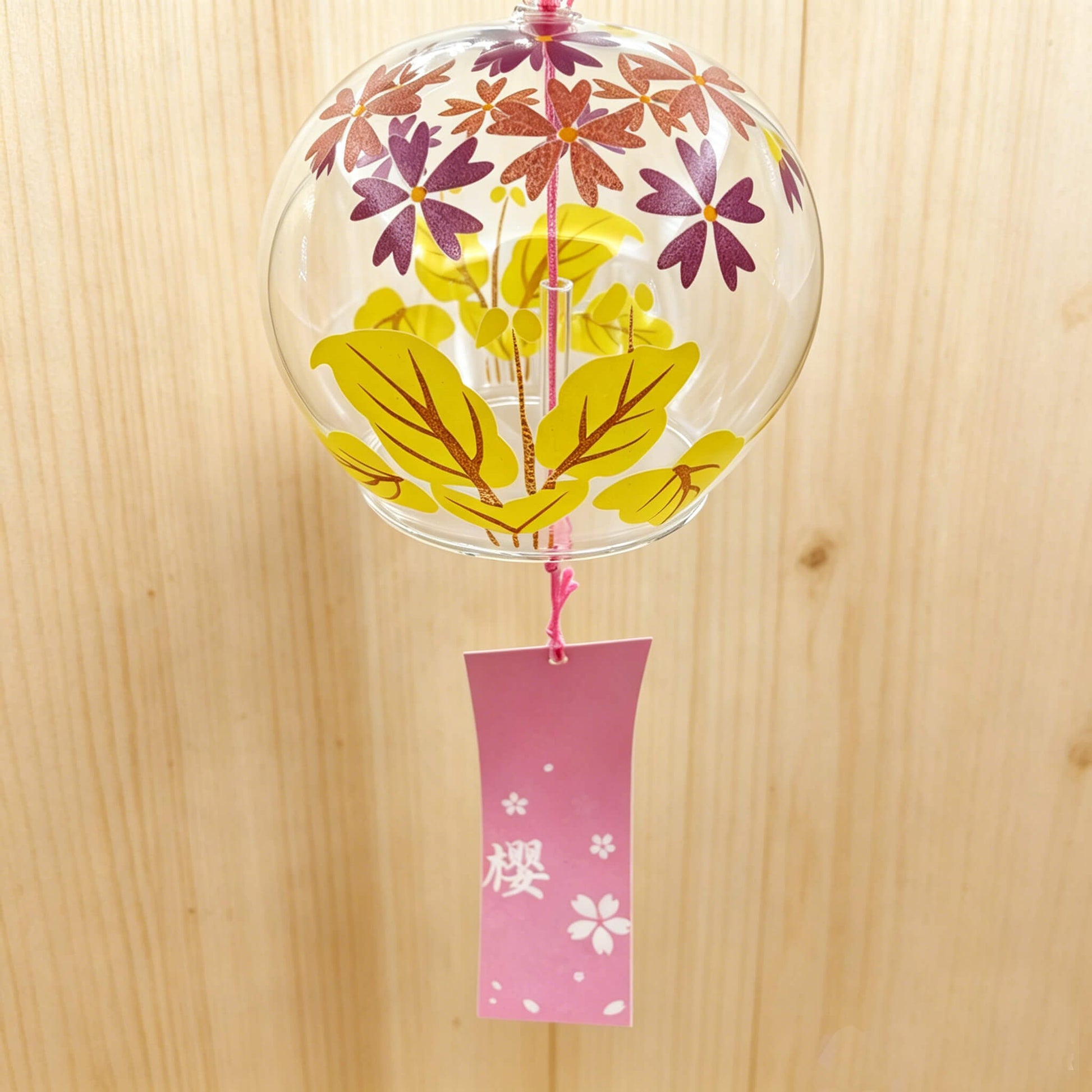 Close-up of Acever autumn maple and sakura glass wind chime X14 showing golden maple leaves and purple star blossoms on clear flat-rim globe with pink cord