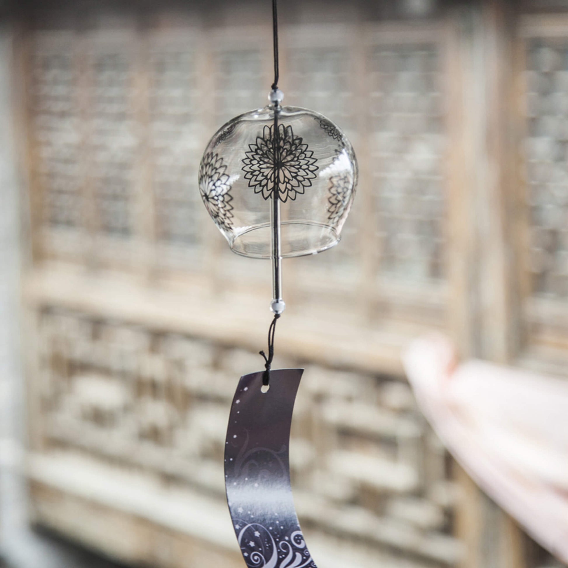 Acever black chrysanthemum mandala glass wind chime X17 hanging against traditional Chinese lattice window showing clear globe with bold black mandala and navy swirl paper strip