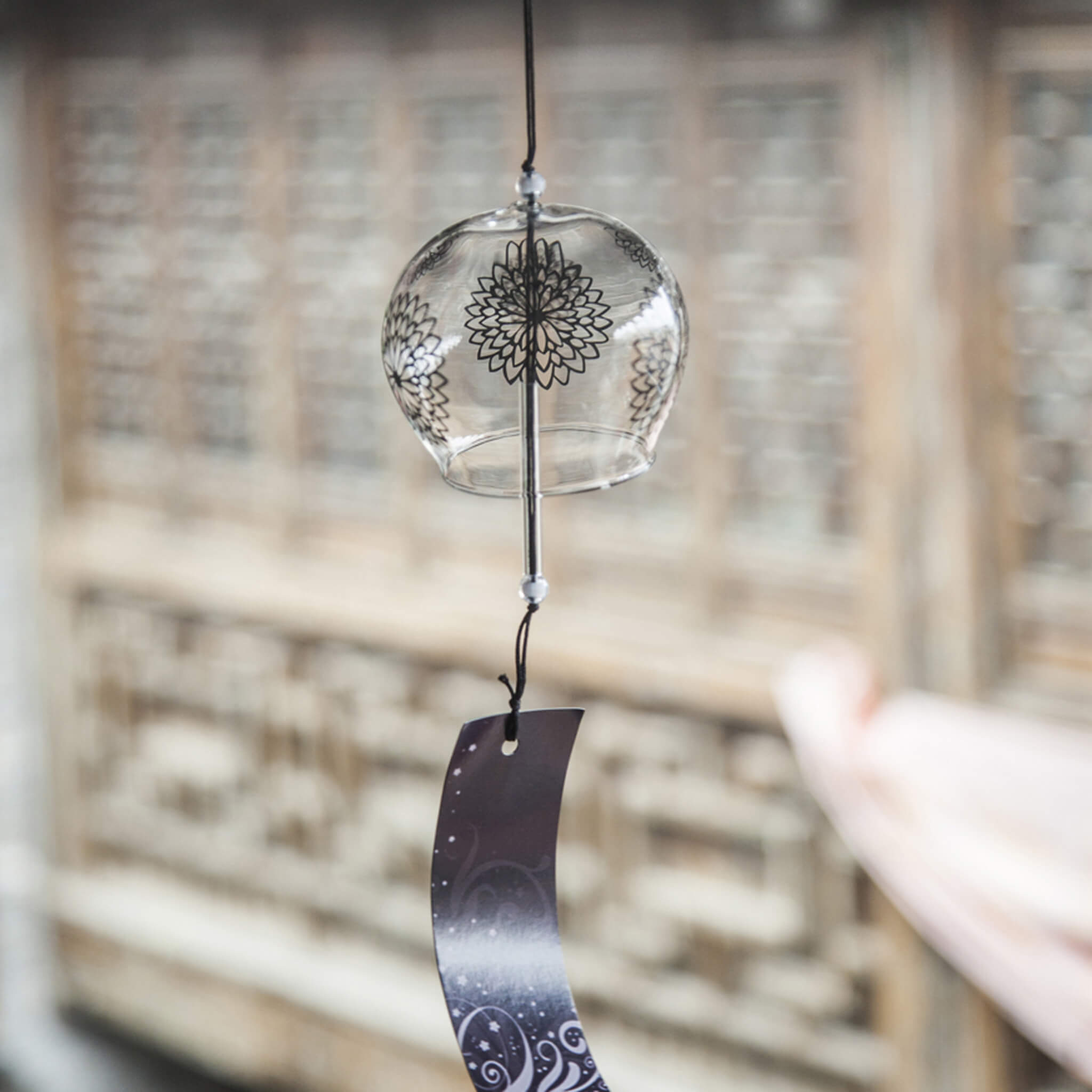 Acever black chrysanthemum mandala glass wind chime X17 hanging against traditional Chinese lattice window showing clear globe with bold black mandala and navy swirl paper strip