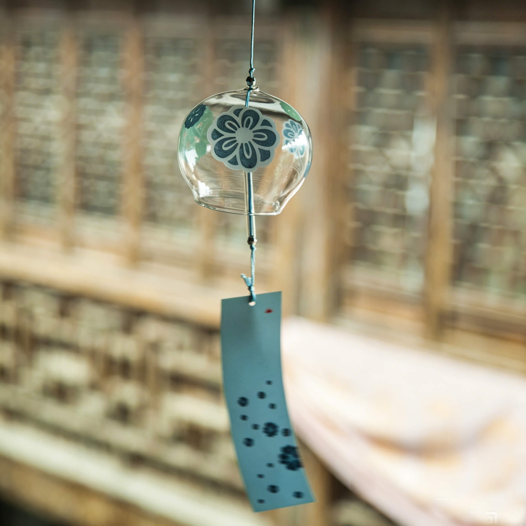 Acever teal plum blossom glass wind chime X19 hanging from traditional Chinese eave in old street showing clear globe with teal ume blossoms and dark slate paper strip swaying