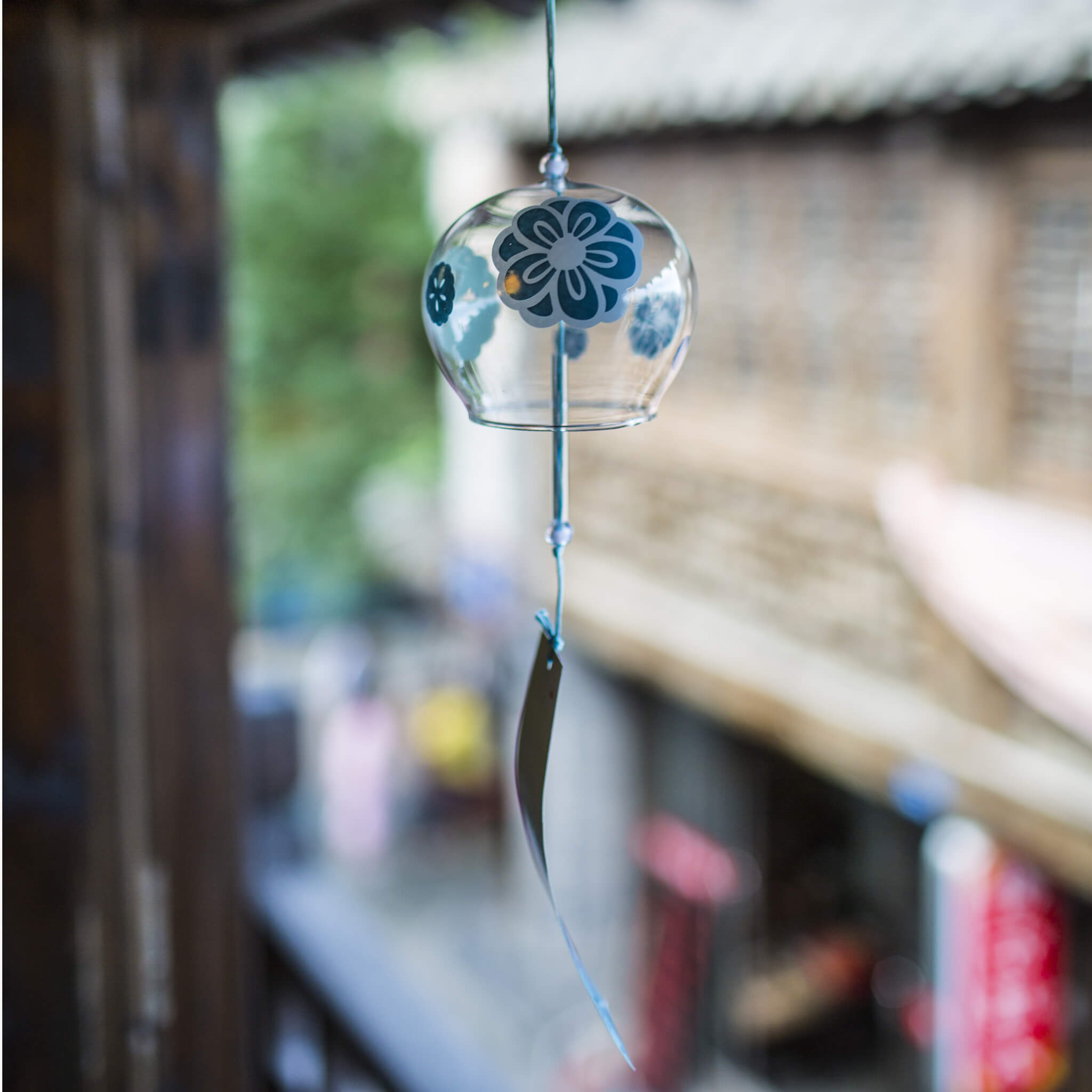Acever teal plum blossom glass wind chime X19 hanging from traditional Chinese eave in old street showing full length with teal ume globe and dark slate plum dot paper strip