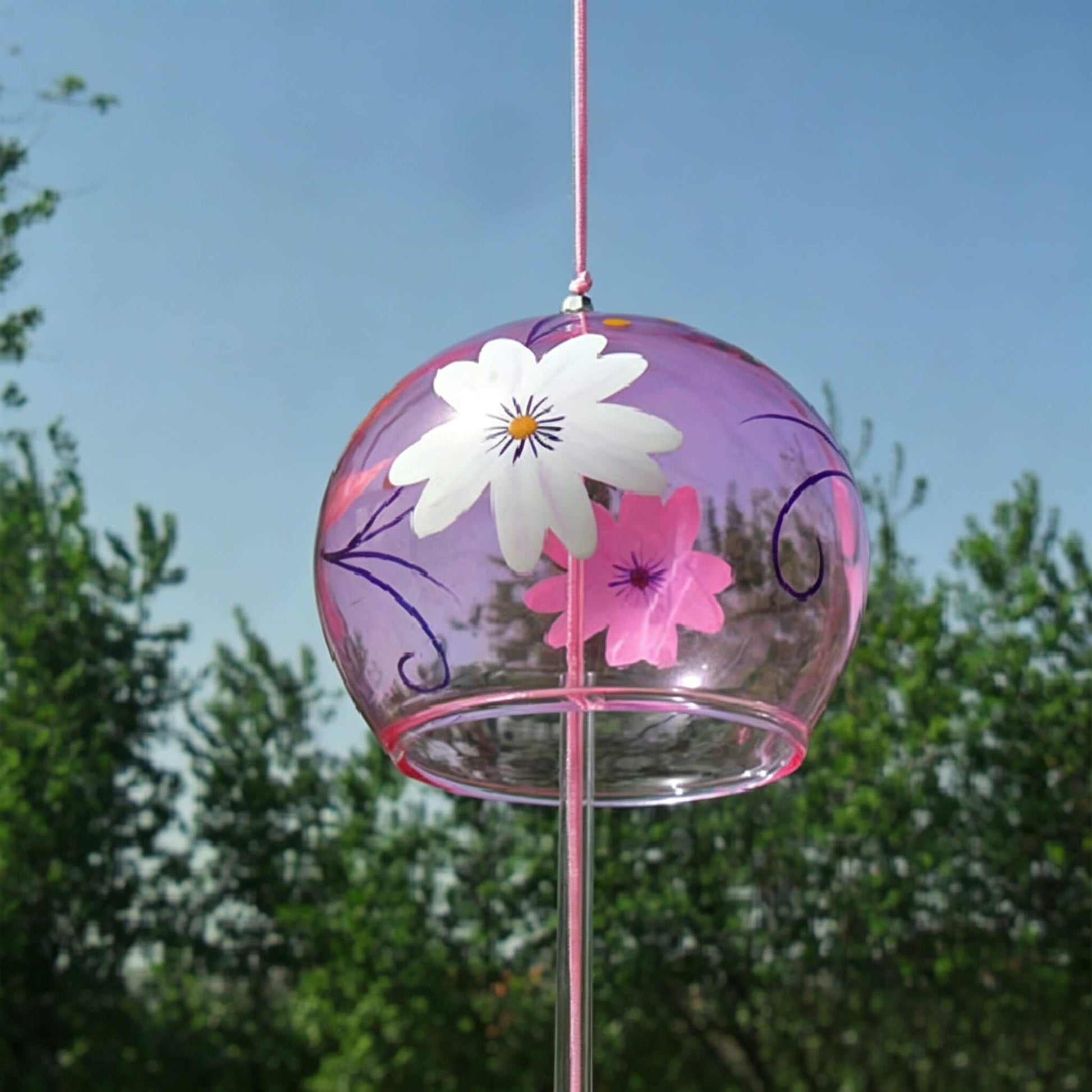 Acever pink sakura glass wind chime X25 hanging outdoors against blue sky showing rose-tinted globe with white sakura blossoms, pink flowers, and navy vine scrolls