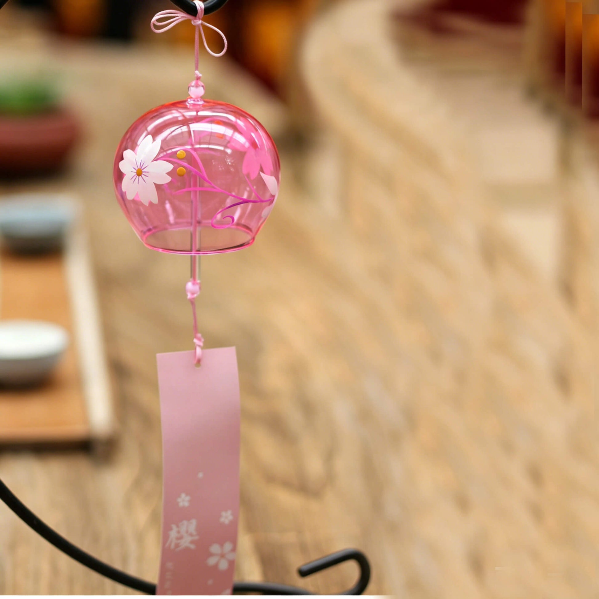 Acever pink sakura glass wind chime X25 hanging on display stand in tea room setting showing rose-tinted globe with white sakura blossoms and pink sakura paper strip
