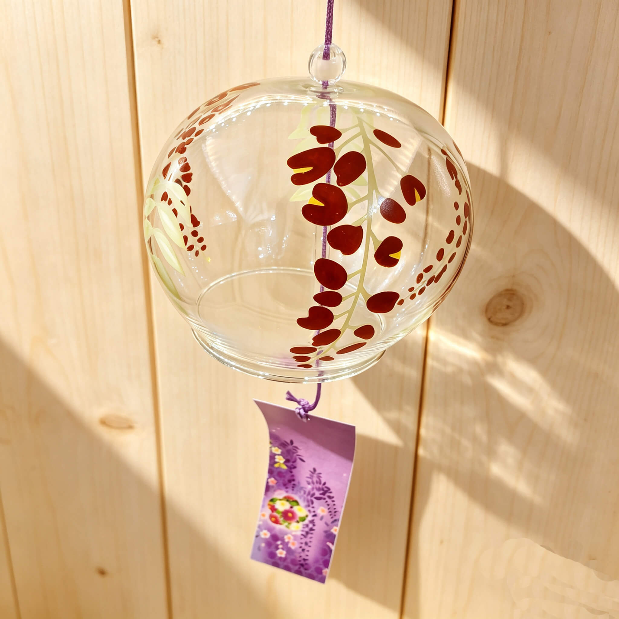 Close-up of Acever purple wisteria glass wind chime X30 on white background showing clear globe with cascading burgundy wisteria petal clusters and lavender paper strip with purple wisteria and floral wreath