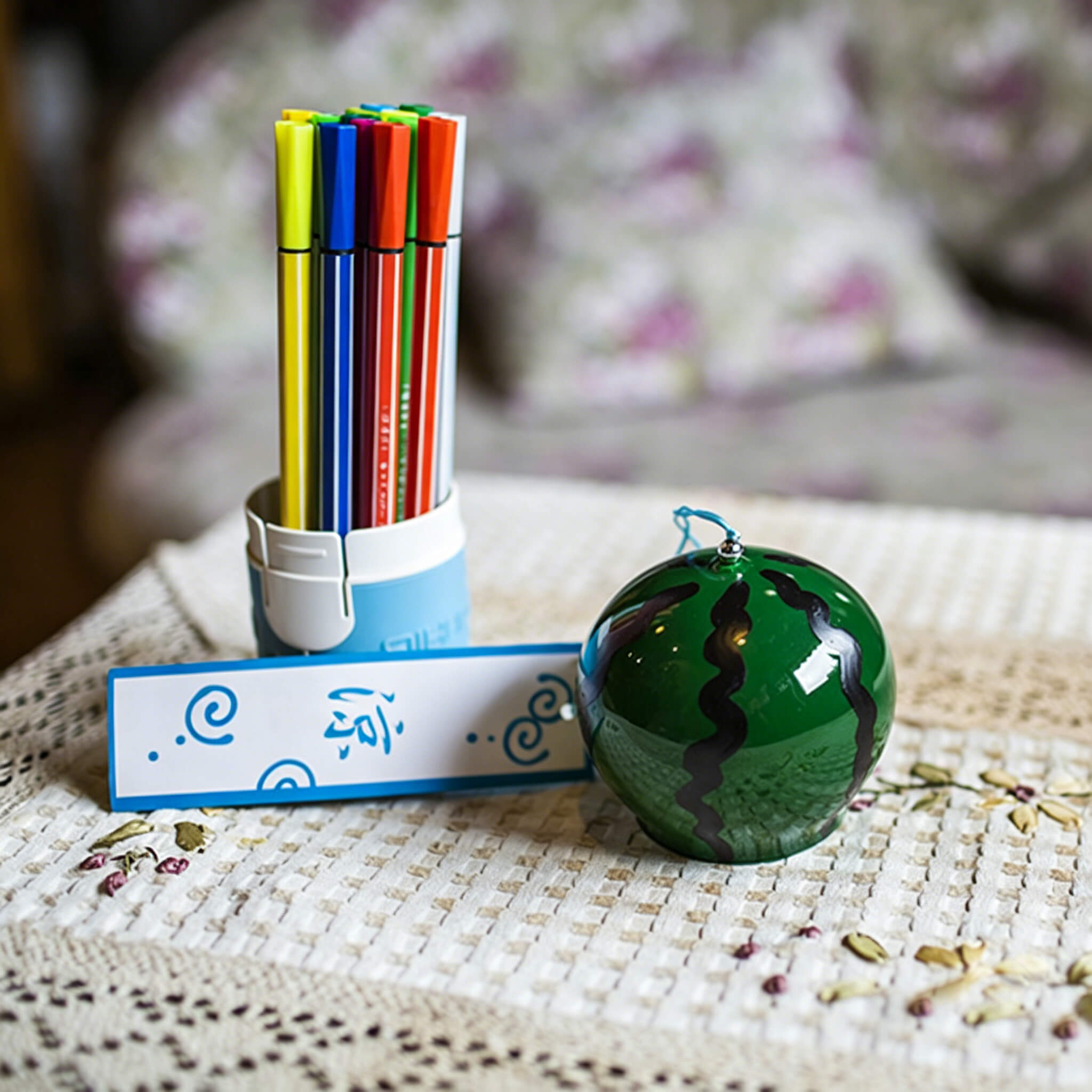 Acever watermelon glass wind chime X31 resting on woven mat next to colourful markers showing deep green globe with bold black wavy stripes and blue paper strip
