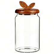 Clear smooth glass jar with round wooden lid featuring carved double leaf handle.