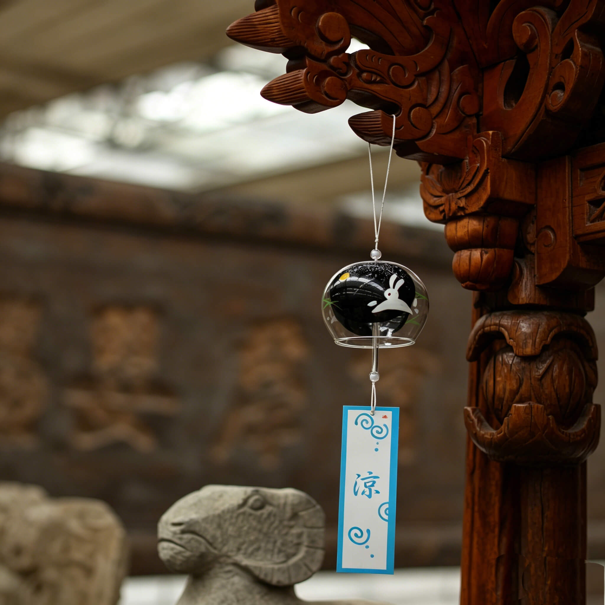 Acever Moon Rabbit glass wind chime X36 hanging from traditional Chinese carved wooden pillar with stone ram showing clear globe with black night sky interior, white rabbit silhouette, and gold moon