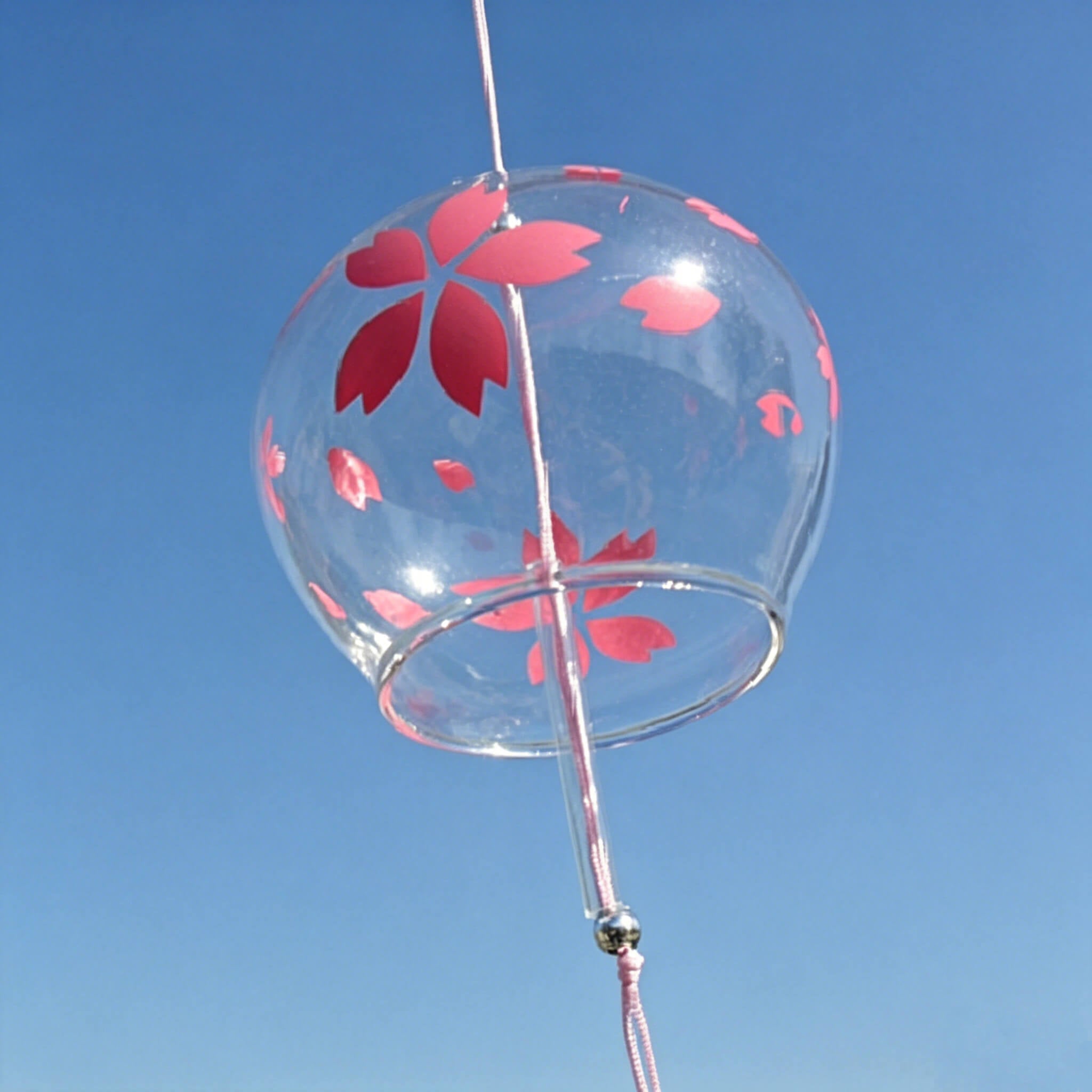 Close-up of Acever red sakura glass wind chime X37 on blue sky background showing clear globe with large red sakura bloom and scattered petals with pink cord and glass beads