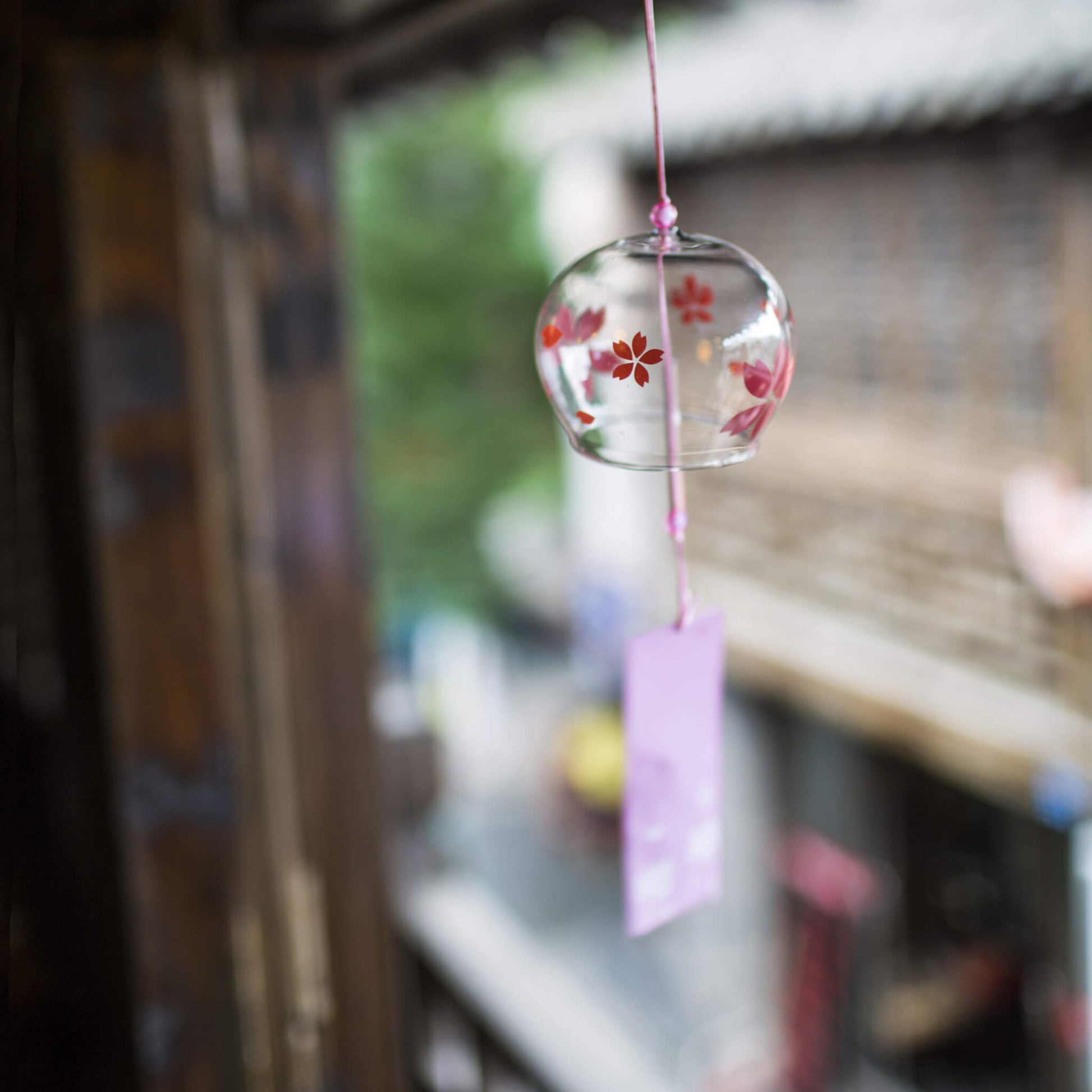 Acever red sakura glass wind chime X37 hanging from traditional Japanese wooden eave in old street showing globe with vivid red cherry blossom blooms and lavender paper strip