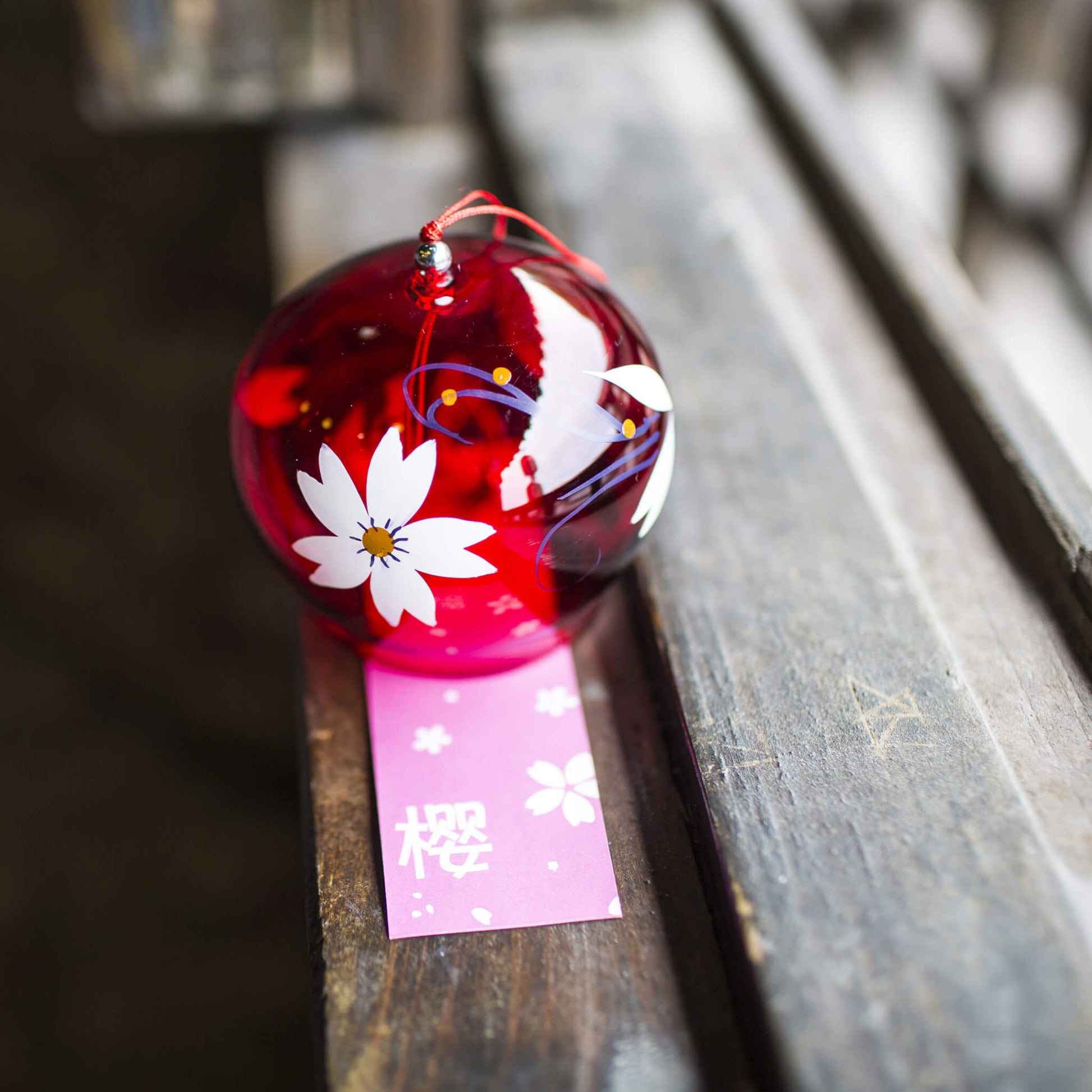 Acever ruby red sakura glass wind chime X38 resting on woven mat next to colourful markers showing deep crimson tinted globe with white sakura blossom and pink sakura paper strip with kanji