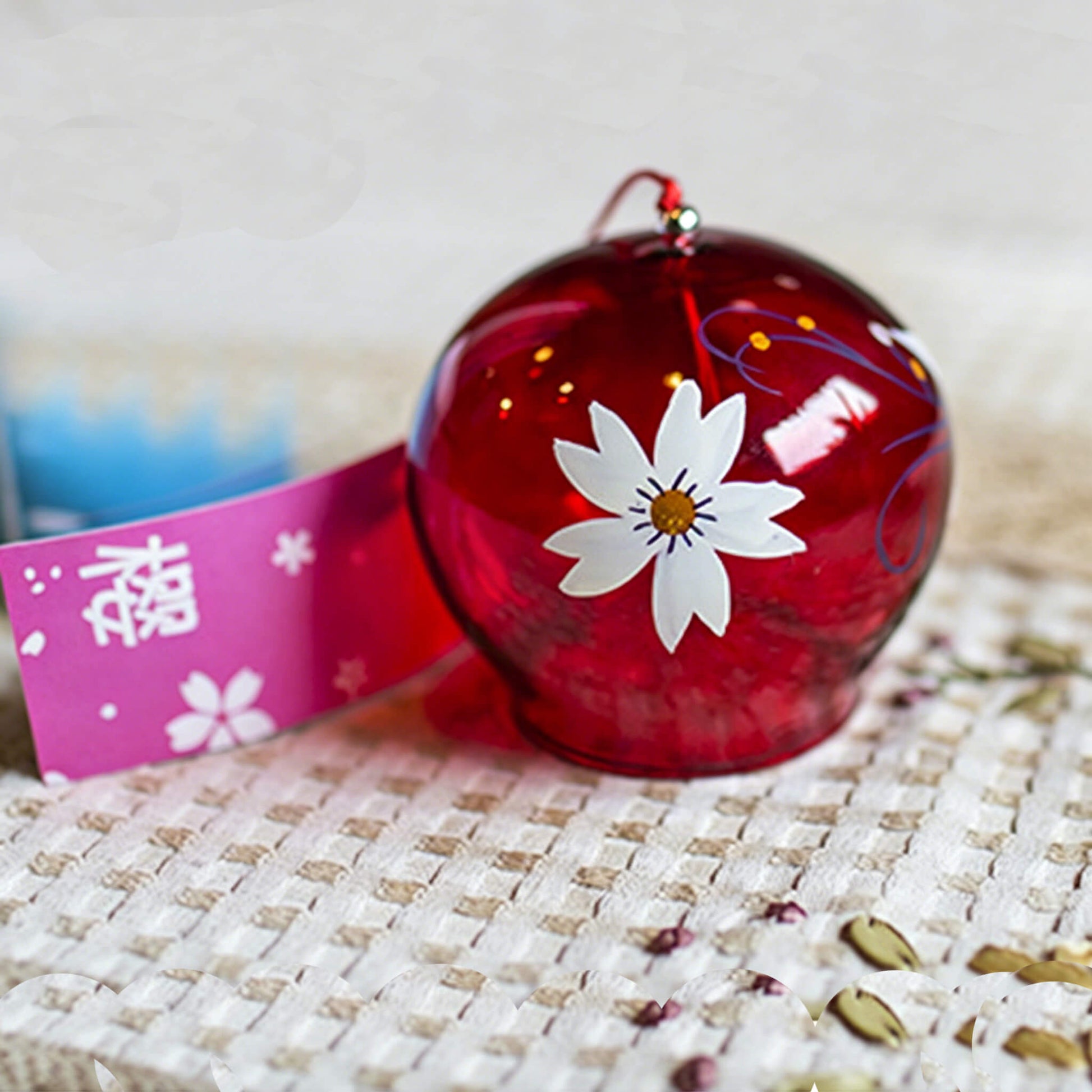 Detail view of Acever ruby red sakura glass wind chime X38 on white background showing crimson tinted globe with white sakura blossom, navy vine scrolls, gold dot accents, and pink sakura paper strip with kanji