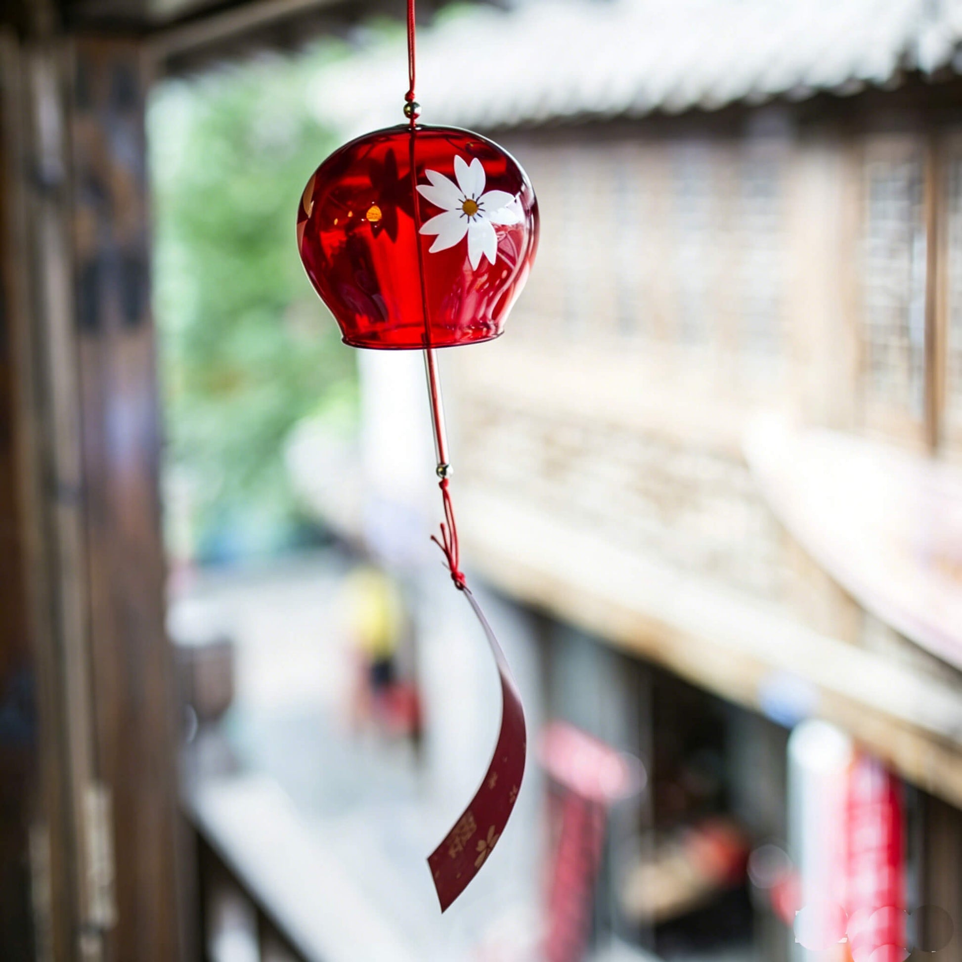Acever ruby red sakura glass wind chime X38 hanging from traditional Japanese wooden eave in old street showing deep crimson tinted globe with white sakura blossom and pink paper strip