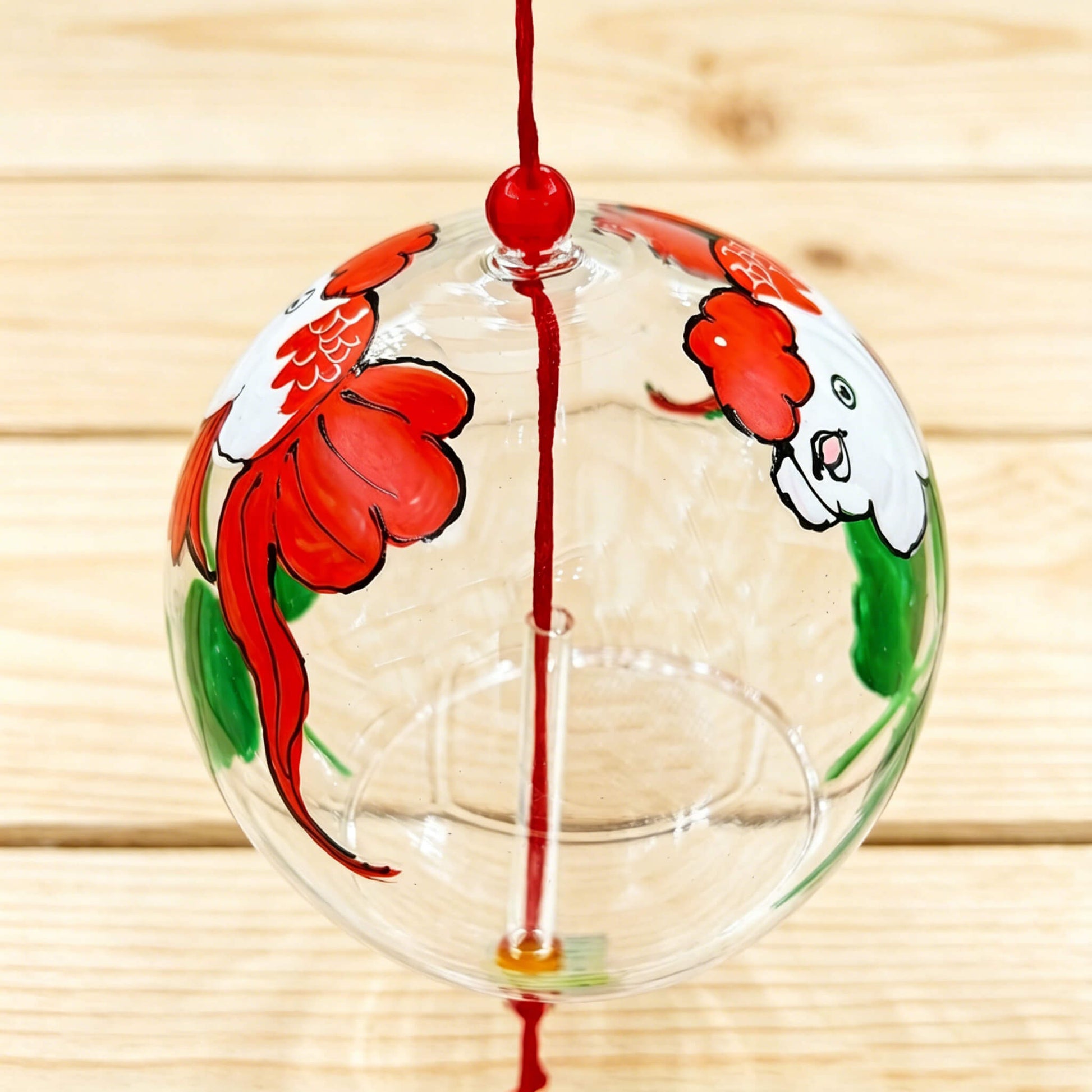 Left view of Acever goldfish glass wind chime X39 on wooden plank surface showing clear ribbed globe with red goldfish and white goldfish swimming with green lotus leaves and red cord with red bead