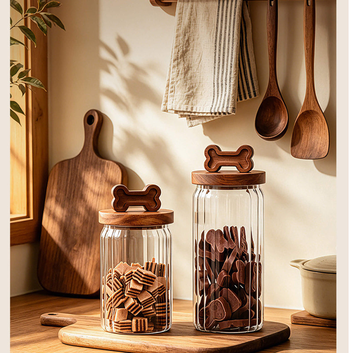 Two ribbed glass jars with bone-handle lids on wooden cutting board next to kitchen utensils.