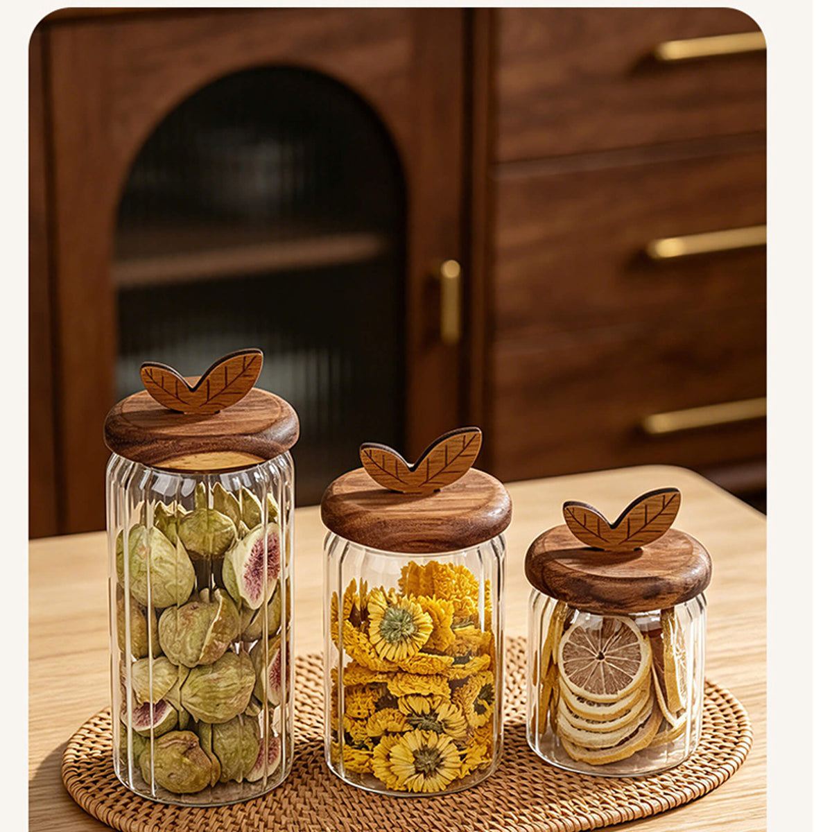 Open ribbed glass jar on side spilling dried figs next to jars filled with flower tea and dried lemon slices.